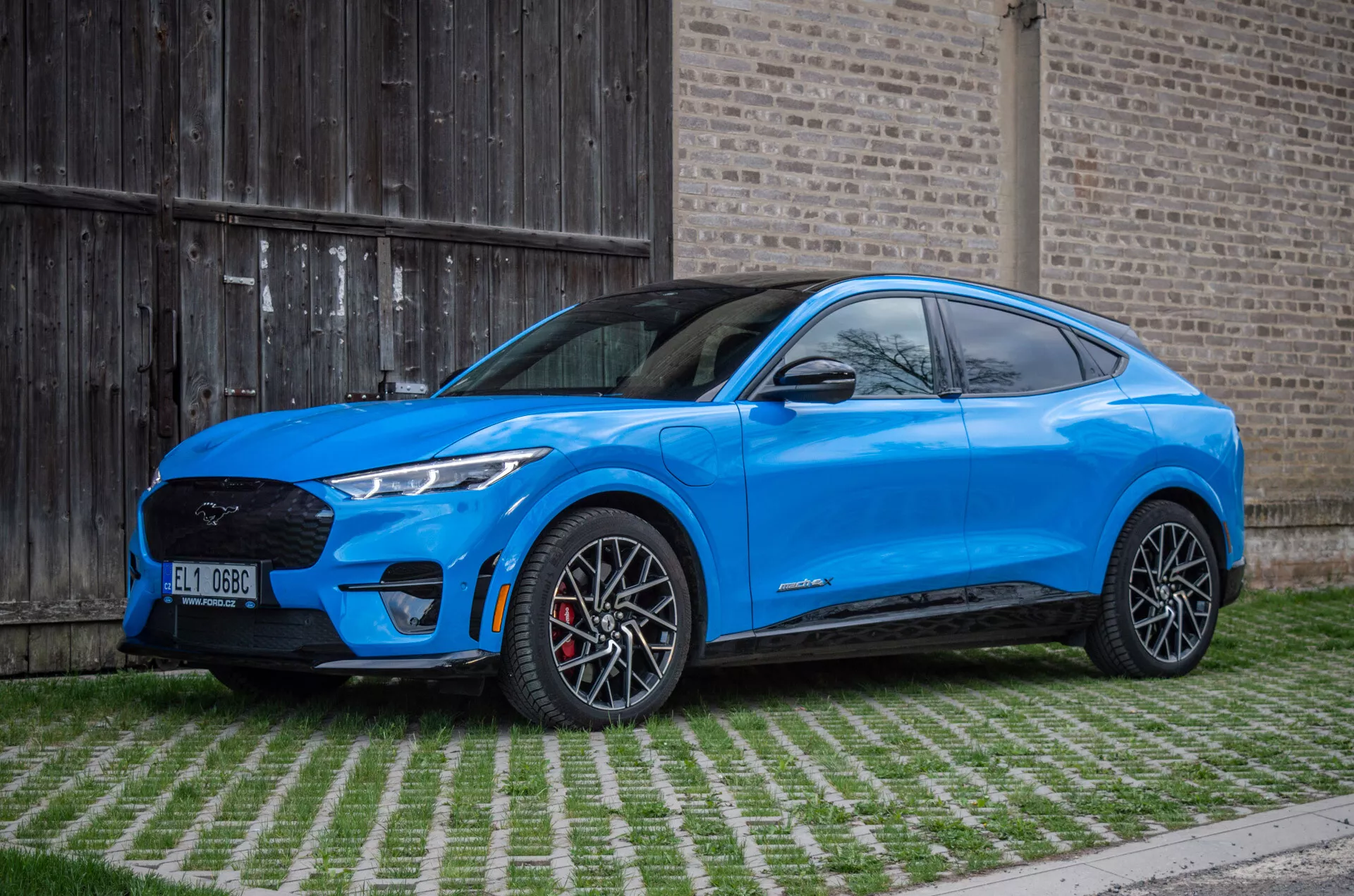 Ford Mustang Mach-E 2020 in blu brillante che mostra il profilo laterale con grandi ruote in lega, fari LED eleganti e design moderno SUV su uno sfondo ecosostenibile