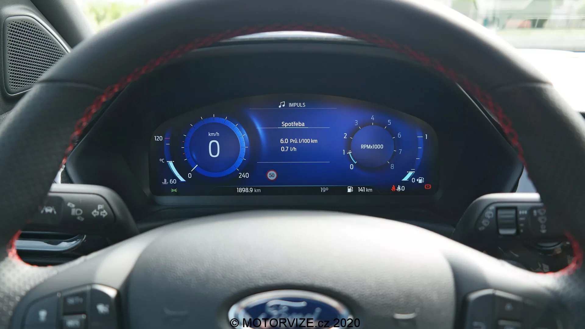 Vista interna della Ford Puma 2020 dal sedile del conducente, con un volante in pelle con pulsanti multifunzione e un cruscotto digitale ad alta risoluzione. Il display mostra velocità, navigazione, metriche del veicolo, indicatore del livello della batteria che suggerisce capacità ibrida/elettrica e controlli per media e cruise control.