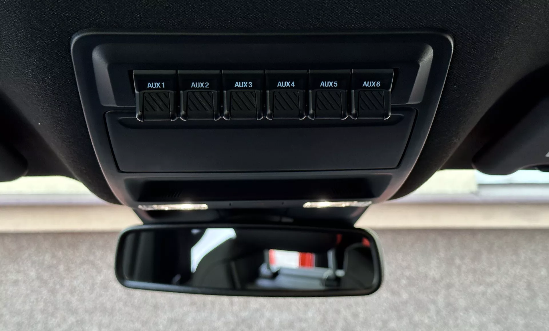 Vista ravvicinata all'interno di un Ford Ranger 2022, con focus sui interruttori ausiliari etichettati da AUX1 a AUX6 sulla console superiore e lo specchietto retrovisore standard dalla prospettiva del guidatore