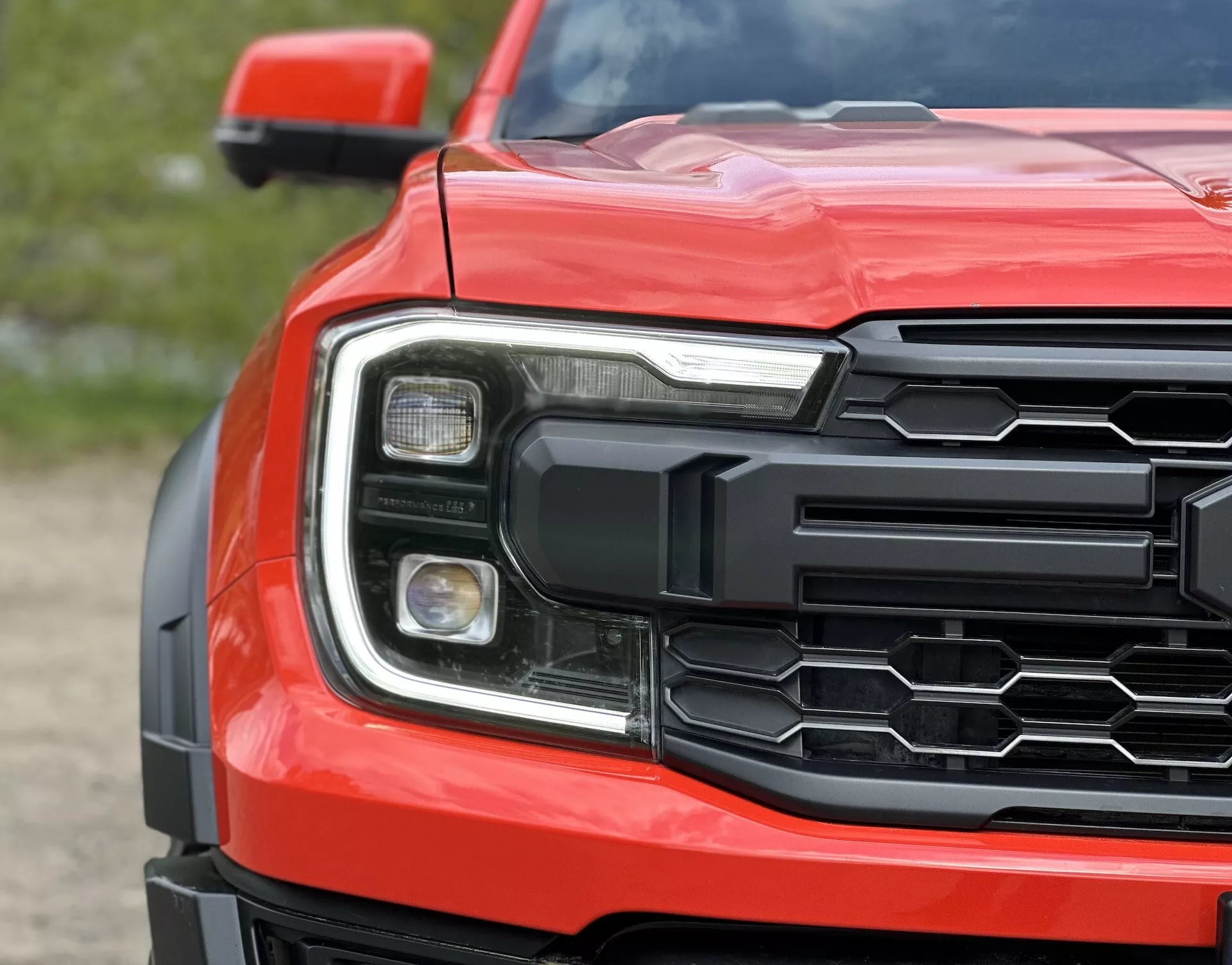 Vista ravvicinata dell'angolo anteriore del Ford Ranger 2022 che mostra griglia esagonale, gruppo ottico dettagliato e cofano sagomato in rosso