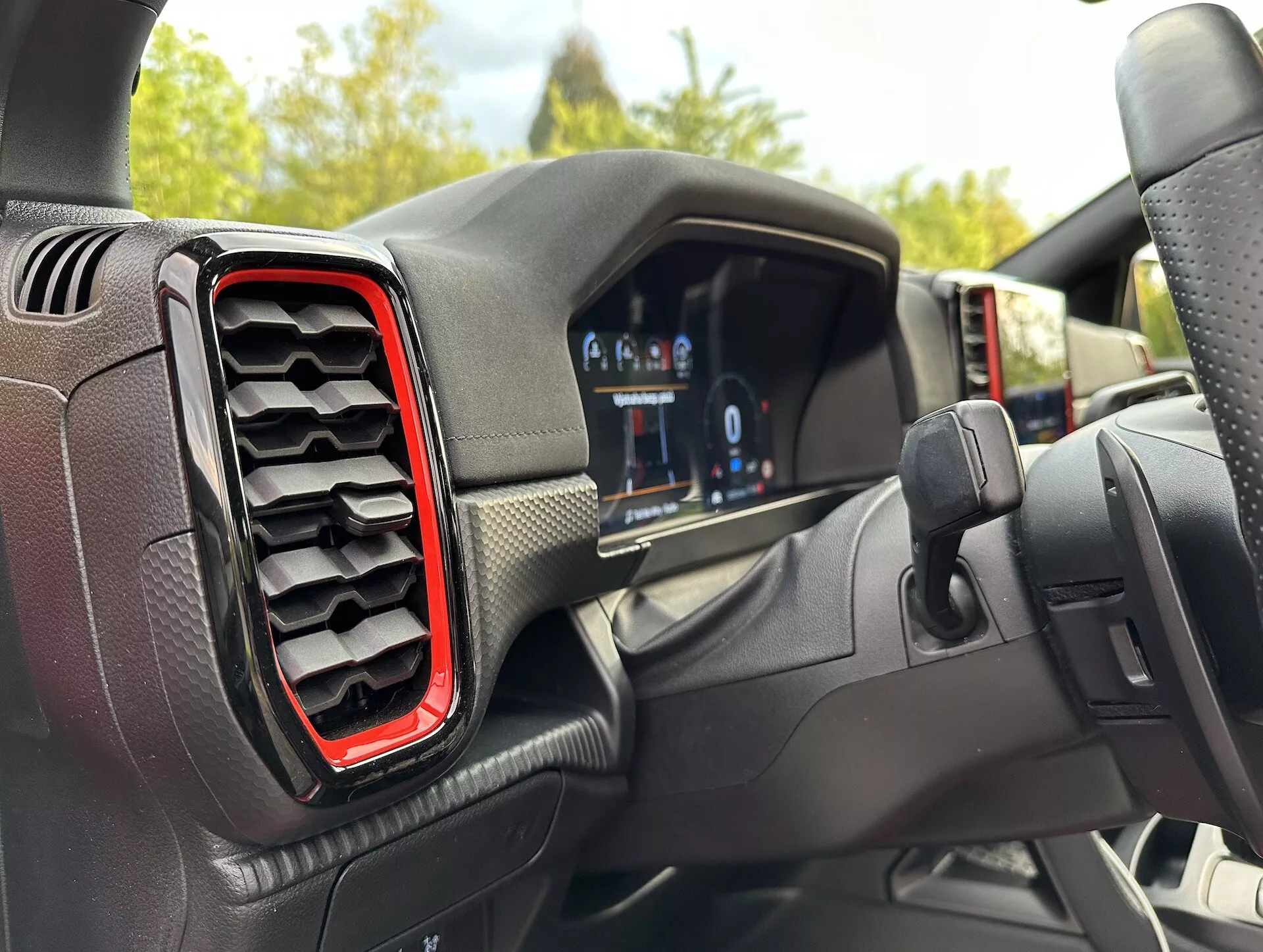 Vista interna del Ford Ranger 2022 dalla prospettiva del conducente, con cruscotto digitale e bocchetta d'aria sinistra con accento rosso, angolata leggermente fuori centro verso il volante suggerendo una svolta