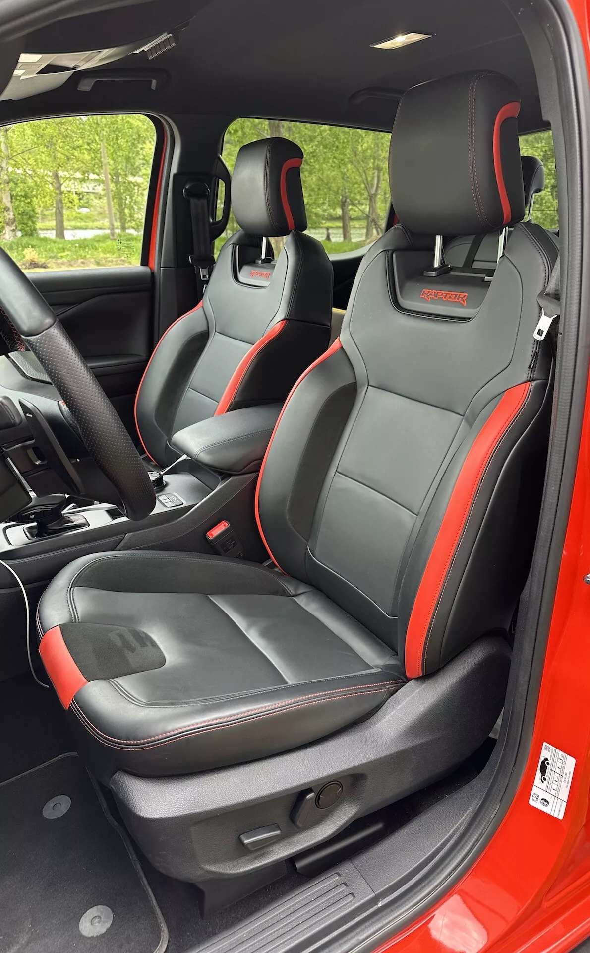 Vista interna del Ford Ranger 2022 focalizzata sui sedili anteriori sportivi con rifiniture accento nero e rosso, funzionalità integrate nei poggiatesta e regolazioni dei sedili elettriche da una prospettiva laterale destra