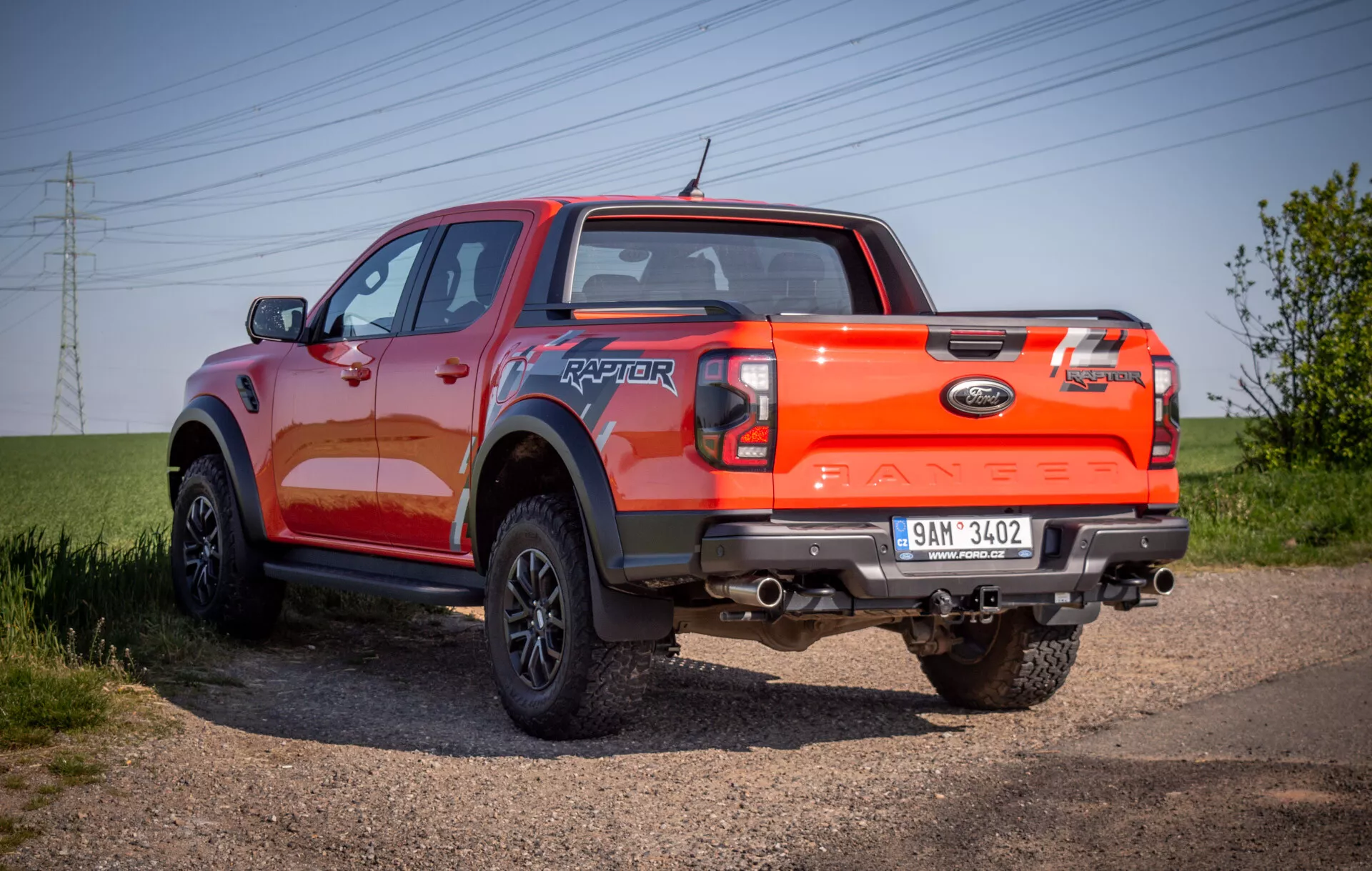 Ford Ranger Raptor del 2022 esposta su un percorso sterrato, evidenziando il suo angolo posteriore trilaterale robusto con un focus sulle capacità fuoristrada e sulla finitura della vernice arancione vivace.