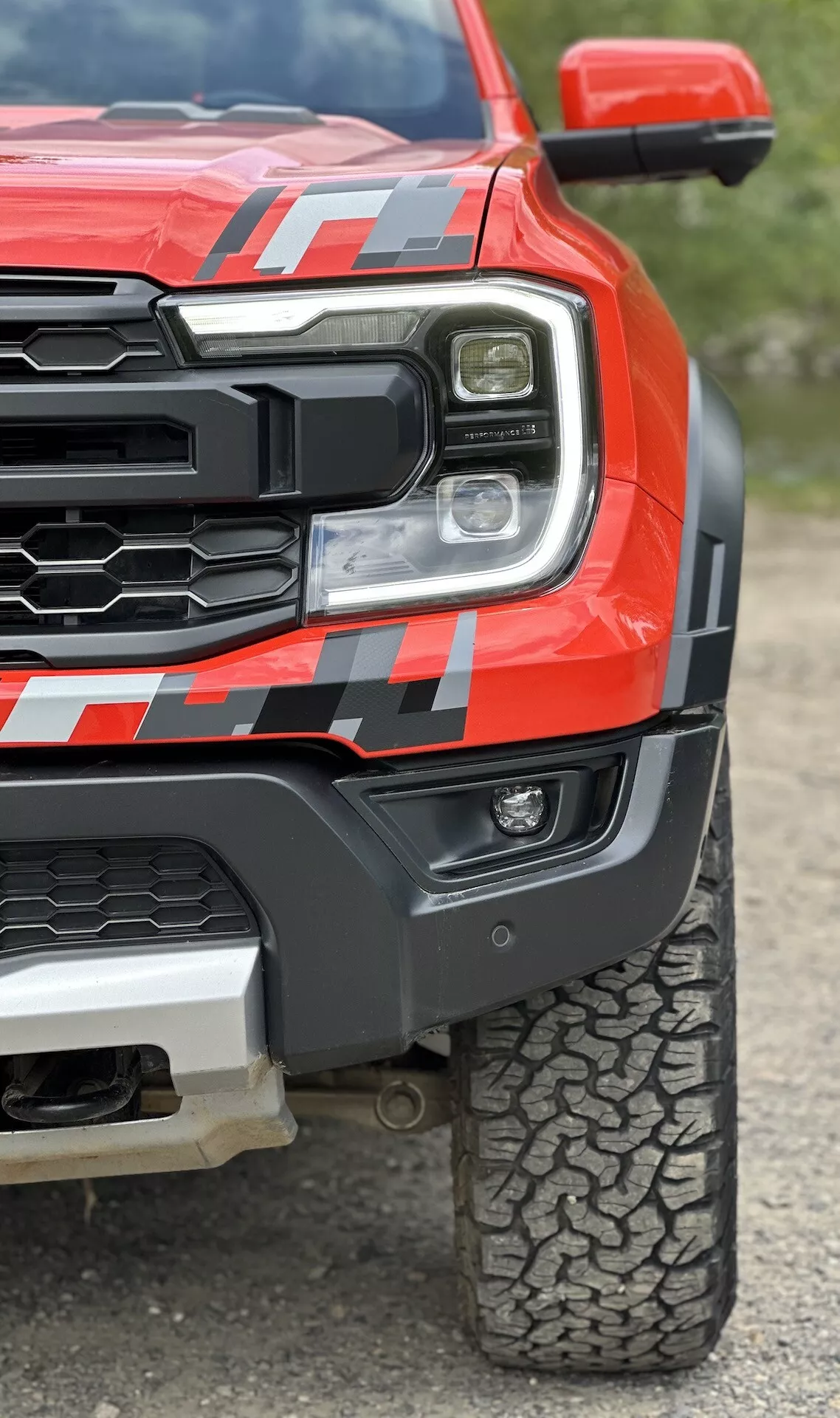 Vista ravvicinata di un pickup Ford Ranger 2022 di colore rosso, che mostra il faro LED, la griglia robusta, il parafango anteriore muscoloso con decalcomania e il disegno del battistrada per fuoristrada da un angolo basso per enfatizzare la robustezza e la tecnologia avanzata