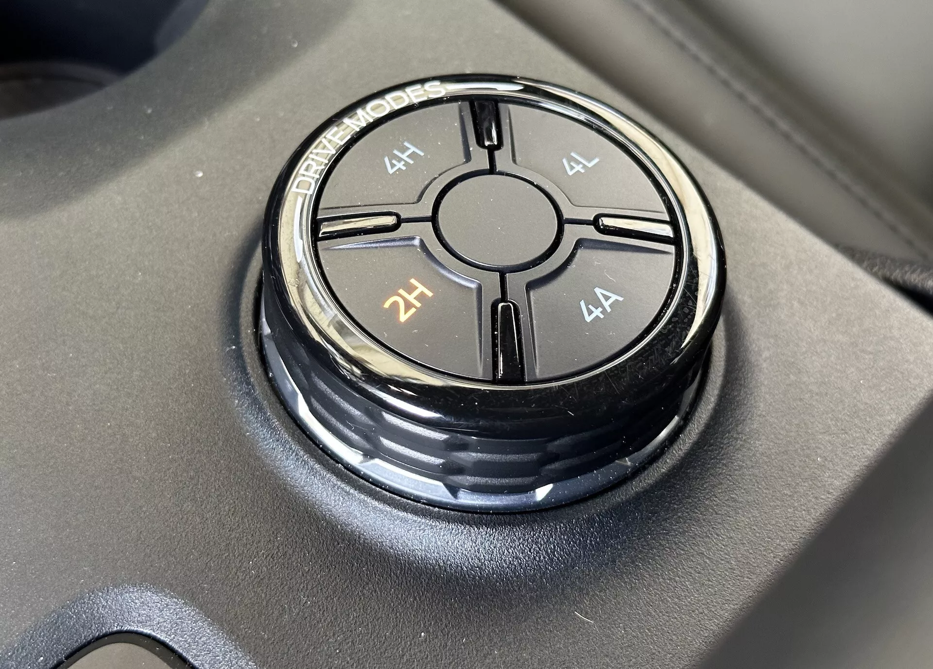 Vista ravvicinata della manopola selettore modalità di guida del Ford Ranger 2022 posizionata su superficie nera opaca, con opzioni 4L, 4H, 2H e 4A evidenziati con una messa a fuoco nitida e riflessione morbida