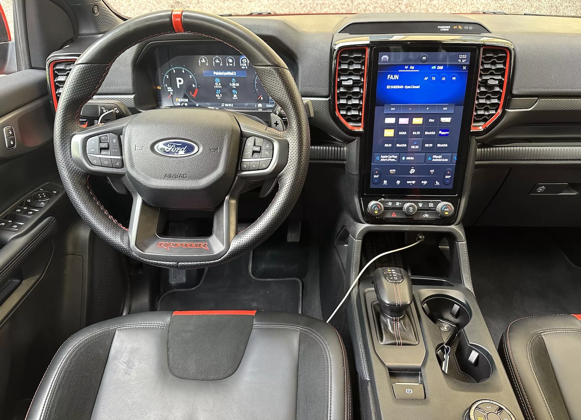 Vista interna della Ford Ranger 2022 dalla prospettiva del conducente, con un volante a tre razze con comandi, quadro strumenti digitale e sistema di infotainment touchscreen verticale sul cruscotto