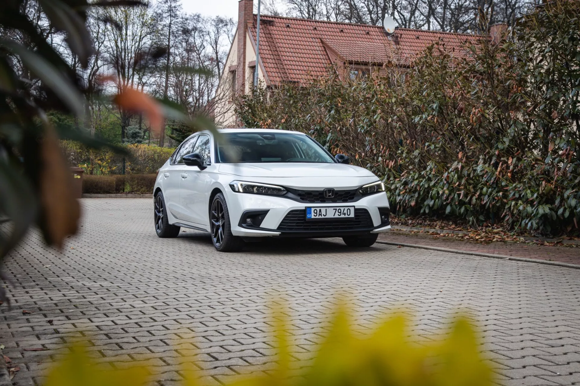 Honda Civic 2022 berlina moderna parcheggiata su un vialetto in ciottoli con paesaggistica e edificio sullo sfondo, mettendo in mostra la griglia frontale, i fari LED e il design aerodinamico elegante