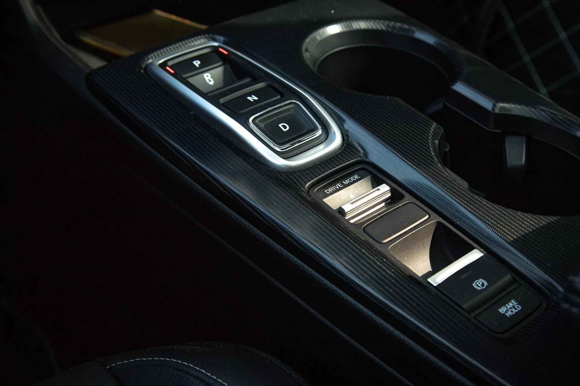Primo piano dell'interno della Honda Civic 2022 della console centrale con selettore elettronico di marcia con pulsanti 'P, R, N, D', pannello con texture in fibra di carbonio e comandi ausiliari, che mostra trasmissione automatica moderna ed estetica sportiva