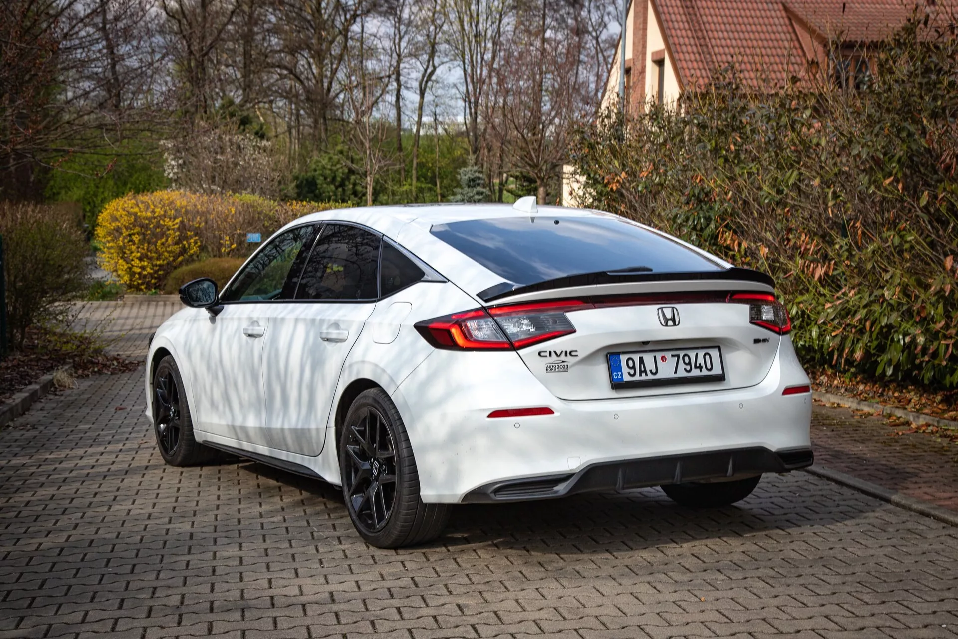 Honda Civic bianca 2022 mostrando il profilo posteriore e parziale laterale su un vialetto in mattoni, con tetto inclinato, spoiler integrato, luce di stop a LED, luci posteriori distintive e paraurti sportivo con diffusore