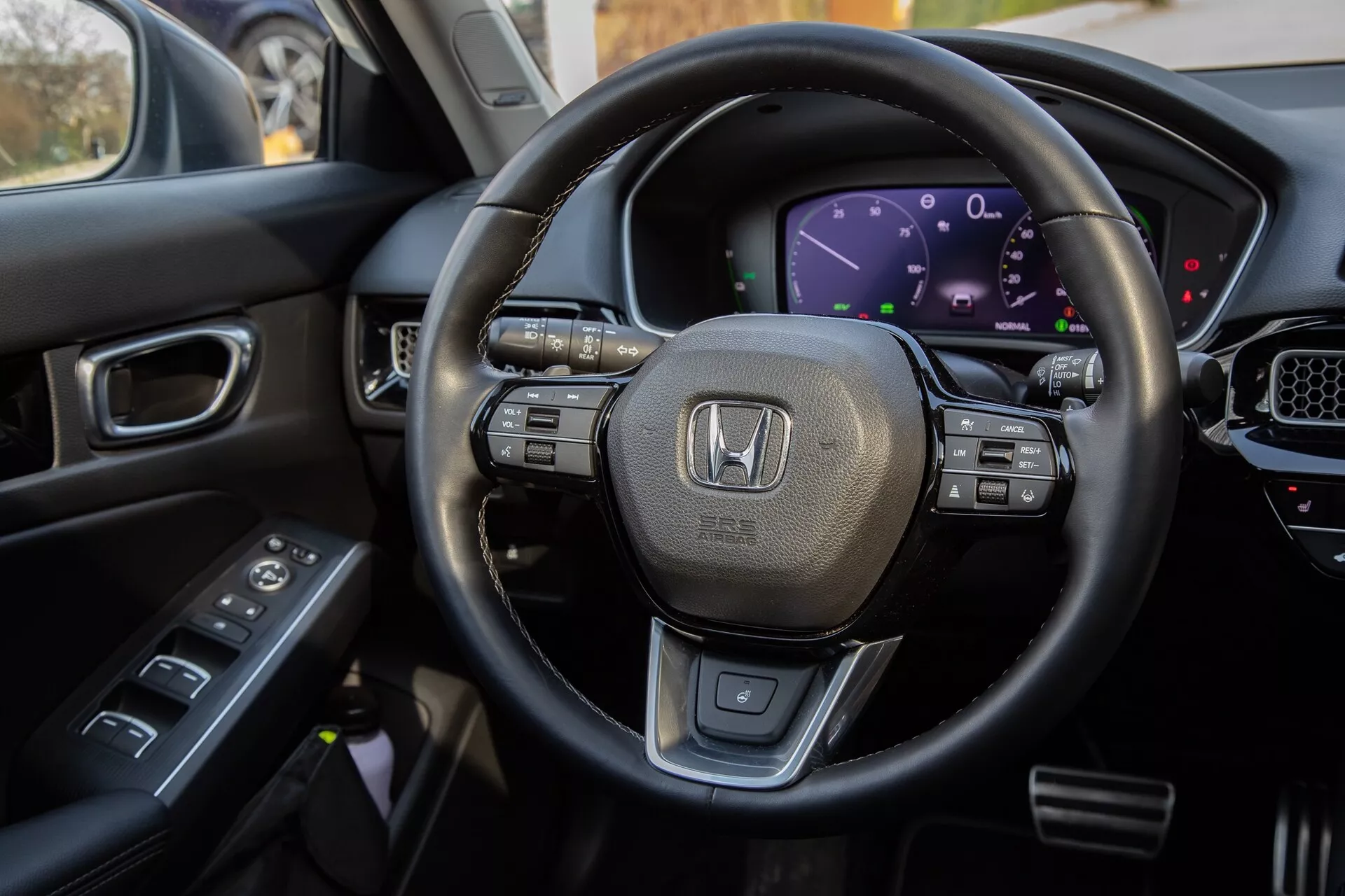Vista interna della Honda Civic 2022 dal sedile del conducente, evidenziando il volante rivestito in pelle con comandi multifunzione, il cruscotto digitale, parte della console centrale con display touchscreen e i comandi sulla porta del conducente per una visualizzazione completa delle moderne caratteristiche tecnologiche e del design di lusso del veicolo.