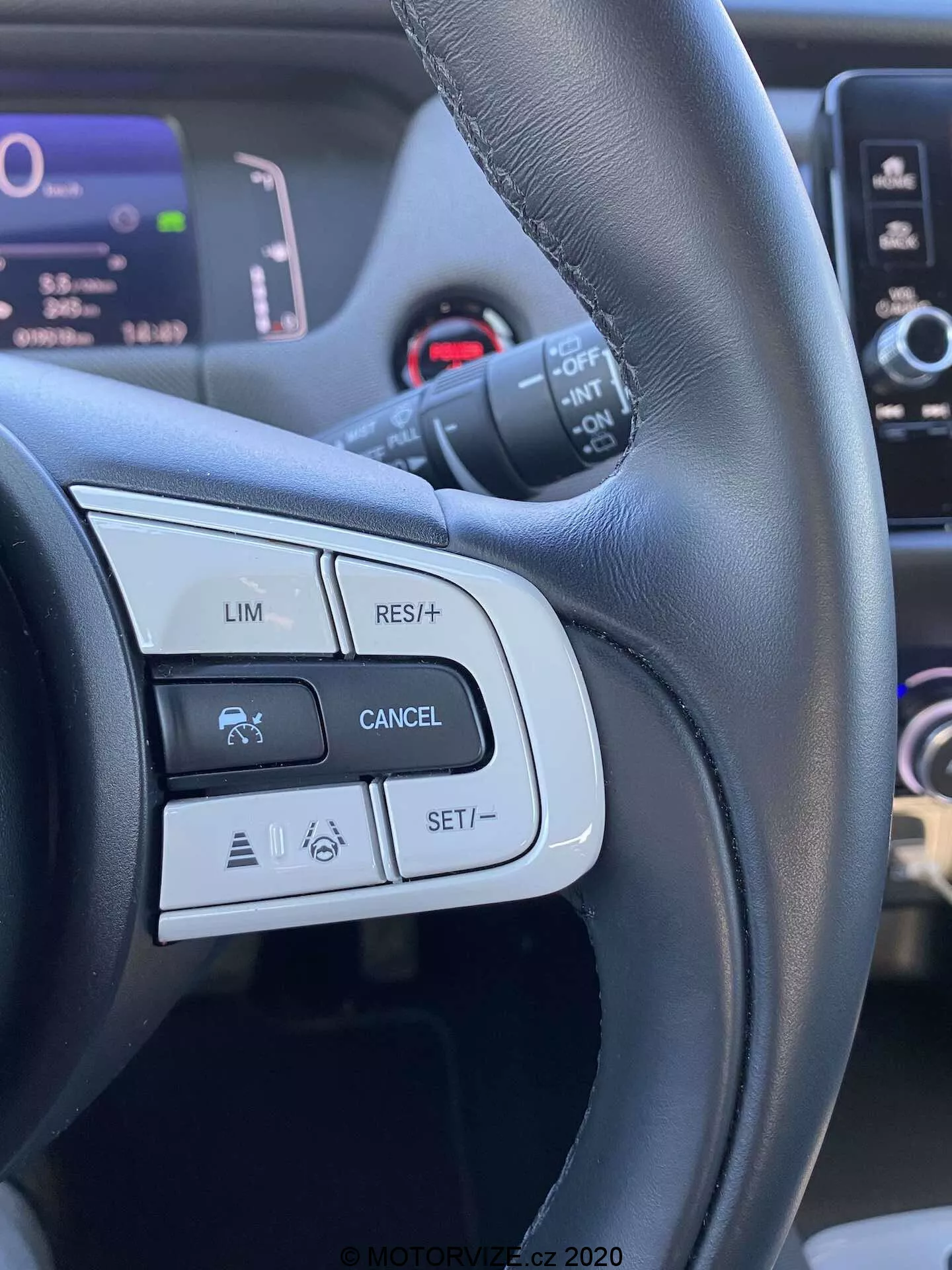 Vista dettagliata dei comandi al volante della Honda Jazz 2020 Crosstar, con particolare attenzione ai pulsanti e alle funzioni sul lato sinistro come LIM (limitazione di velocità), RES/+ (ripresa o aumento della velocità), CANCEL e SET/- (impostazione o diminuzione della velocità). L'immagine è presa dalla prospettiva del conducente, evidenziando un volante in pelle nera con finiture opache e lucide e mostrando icone relative al controllo di crociera e a possibili sistemi avanzati di assistenza alla guida.