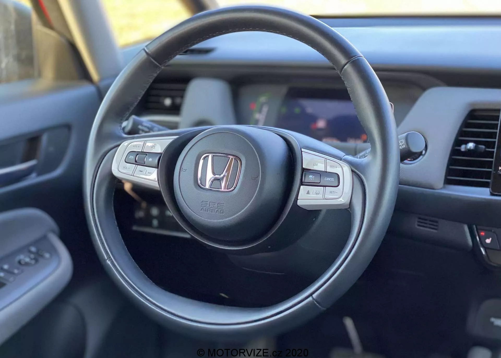 Vista interna della Honda Jazz Crosstar 2020 dalla prospettiva del conducente, focalizzata sul volante moderno con logo Honda, con pulsanti di controllo multifunzione per audio, cruise control e chiamate in vivavoce, e vista parziale del cruscotto e del sistema di infotainment.