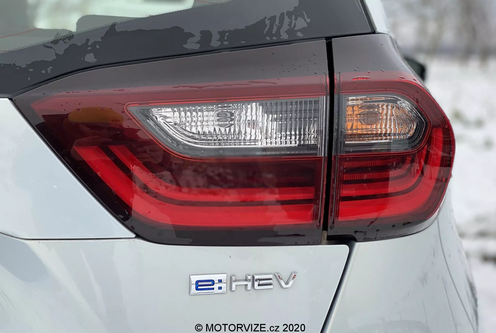Primo Piano Posteriore Honda Jazz 2020: Con Emblema Ibrido 'e:HEV' e Fanale Posteriore LED Moderno. L'immagine evidenzia la carrozzeria grigio-argento con un design intricato delle luci posteriori da un angolo basso di 45 gradi.