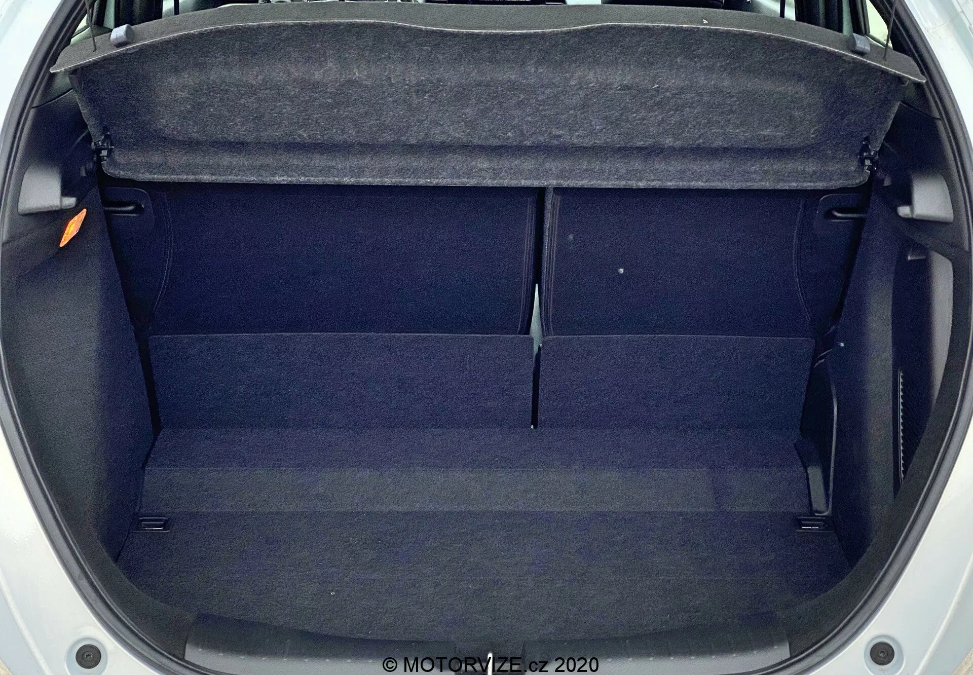Vista dall'alto del bagagliaio vuoto della Honda Jazz 2020, mostrando un vano rettangolare di dimensioni moderate con rivestimento in tessuto scuro. Le caratteristiche includono una mensola all'ingresso, rifiniture interne ai lati e una leggera elevazione al centro. Il bagagliaio è pulito, senza ostruzioni e sembra ben mantenuto.
