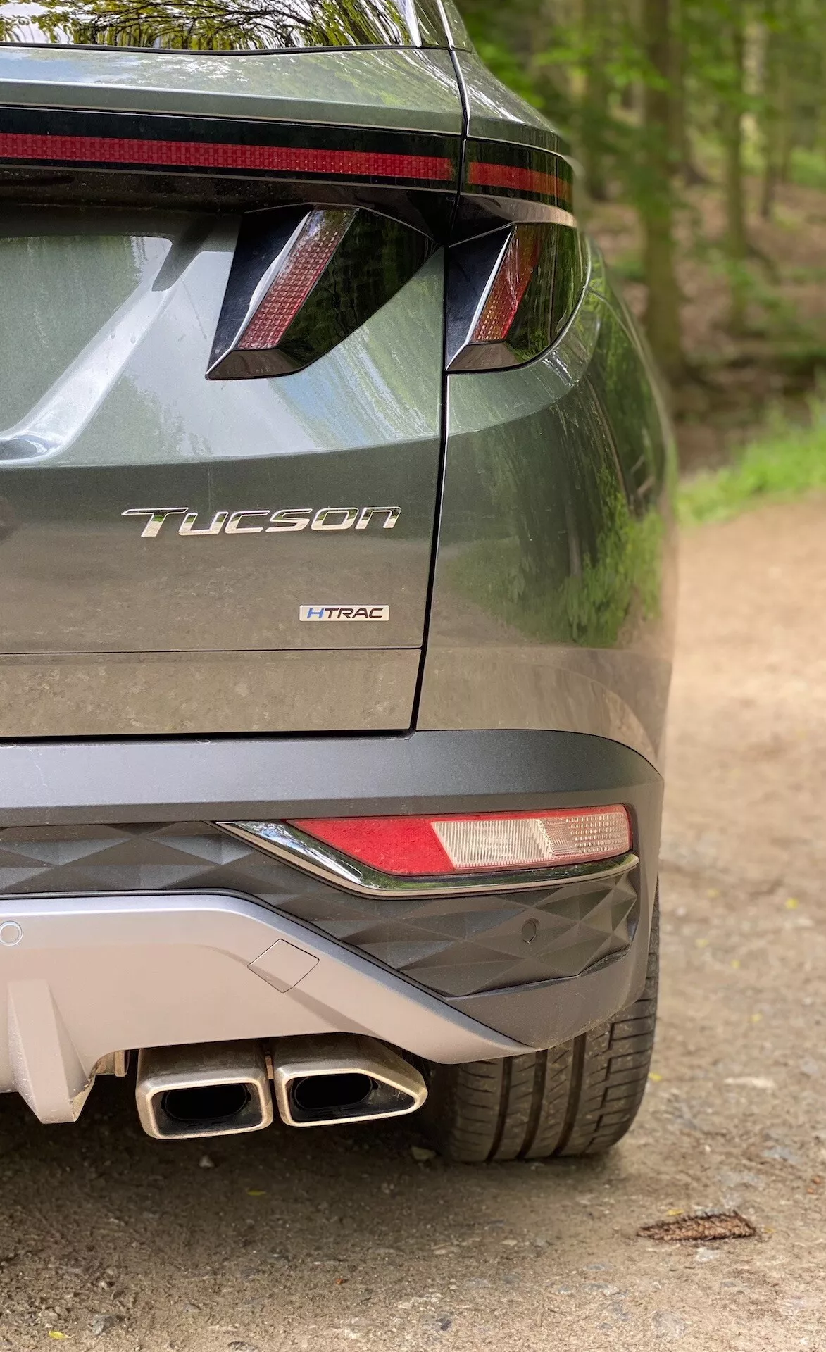 Vista parziale posteriore della Hyundai Tucson modello 2020 che indica che è la versione 1.6 T-GDi Pure, mostrando il lato destro del paraurti, fanale posteriore parziale, spoiler posteriore con luce di stop a LED, doppi terminali di scarico e badge del modello con il nome 'Tucson' e tecnologia del motore 'T-GDi'.