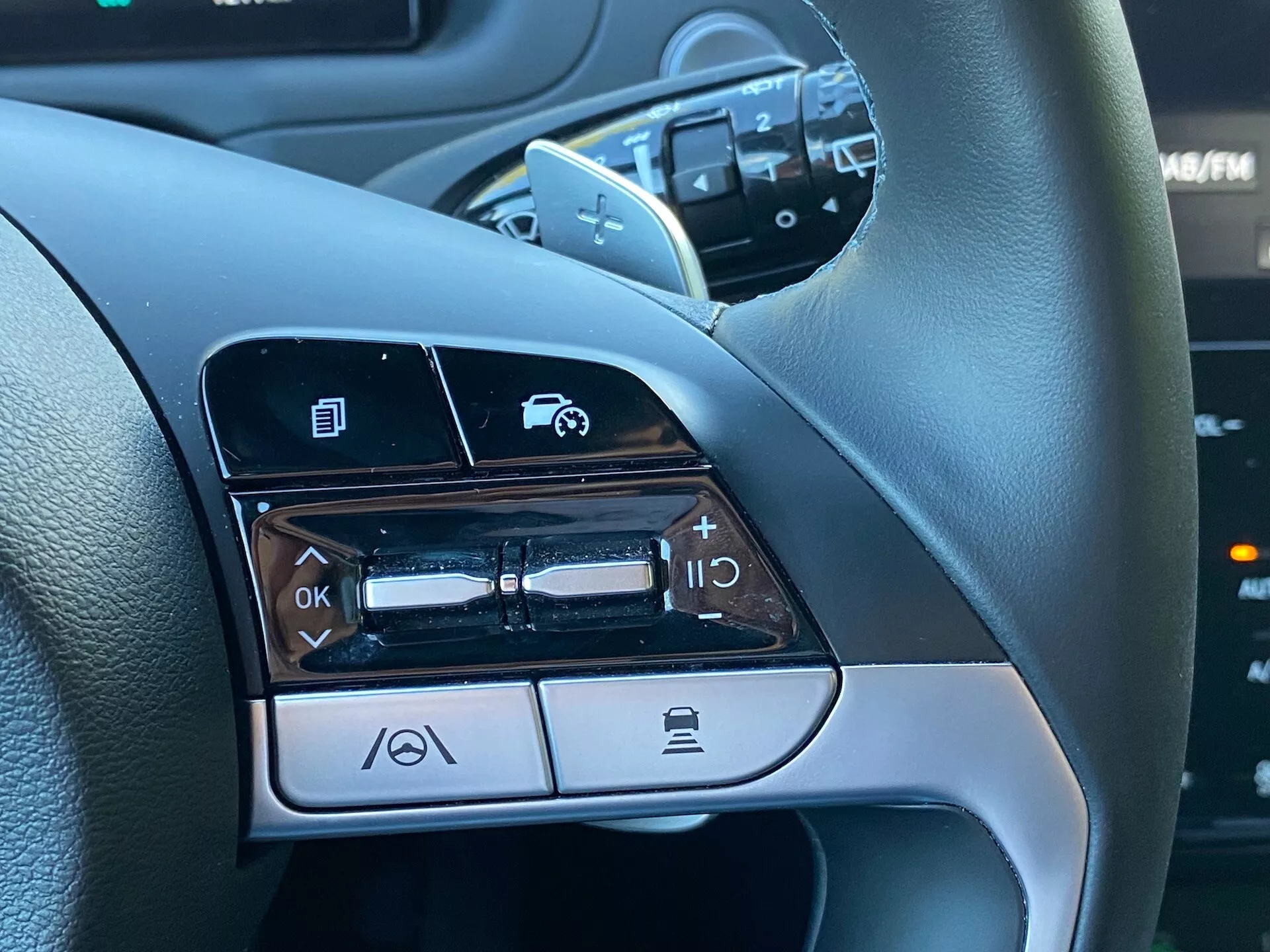 Vista ravvicinata dei comandi montati sul volante sul lato sinistro di una Hyundai Tucson 1.6 T-GDI Pure 2020, che mostra funzionalità come la navigazione nei menu, il controllo del volume audio, l'attivazione dei comandi vocali e la funzionalità di chiamata tramite Bluetooth.