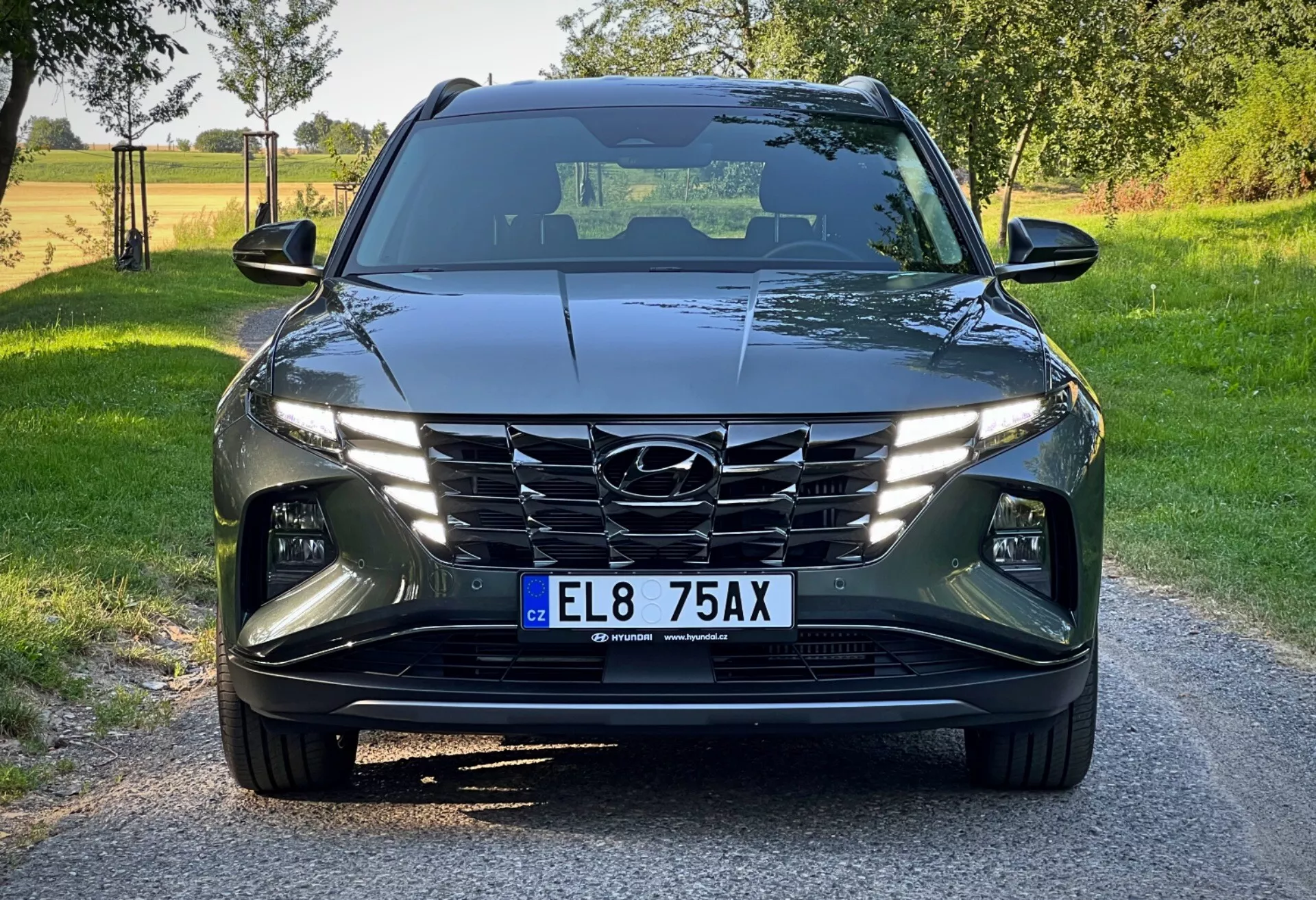 Hyundai Tucson 2020 vista da un angolo basso frontale, mostrando il suo design moderno con linee affilate, fari LED, griglia a cascata e sistemi avanzati di assistenza alla guida in una luminosa ambientazione rurale diurna