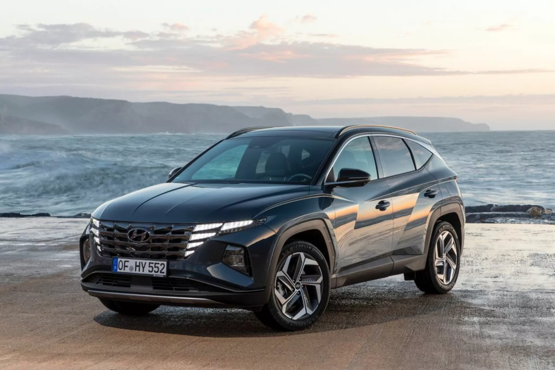 SUV moderno Hyundai Tucson 2020 parcheggiato su un lungomare con orizzonte e oceano sullo sfondo, mostrando la sua vista frontale a tre quarti che evidenzia il design del veicolo, la griglia prominente con logo, fari LED angolari e ruote in lega sportive