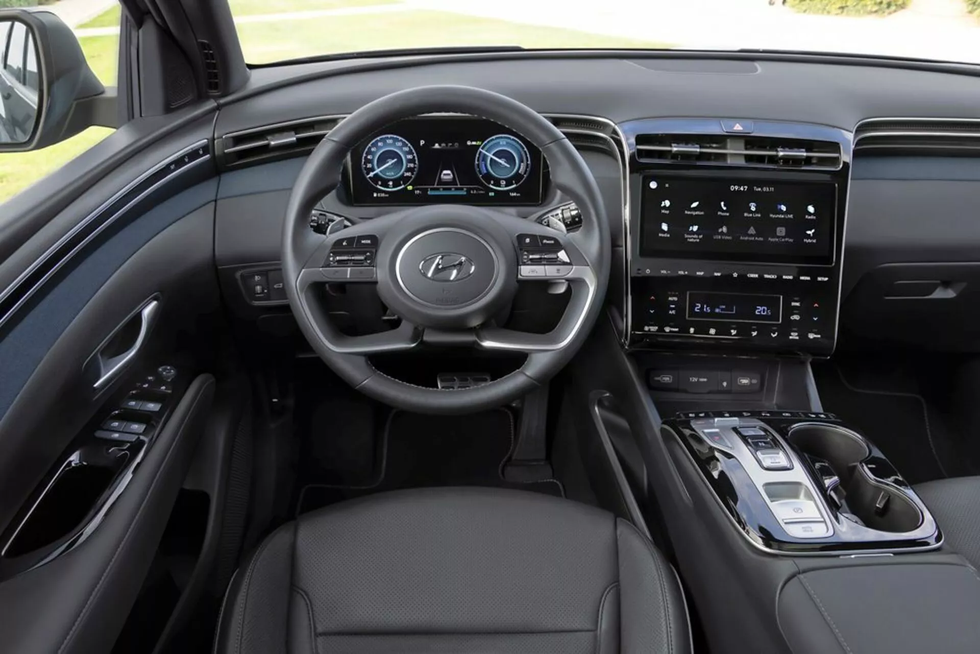 Vista interna del Hyundai Tucson 2020 dalla prospettiva del conducente, mettendo in evidenza cruscotto, volante multifunzione con logo Hyundai, quadro strumenti digitale, sistema di infotainment con schermo touch verticale, controlli minimalisti sulla console centrale, selettore di marcia elettronico, rivestimenti in pelle e sofisticato schema di colori monocromatico