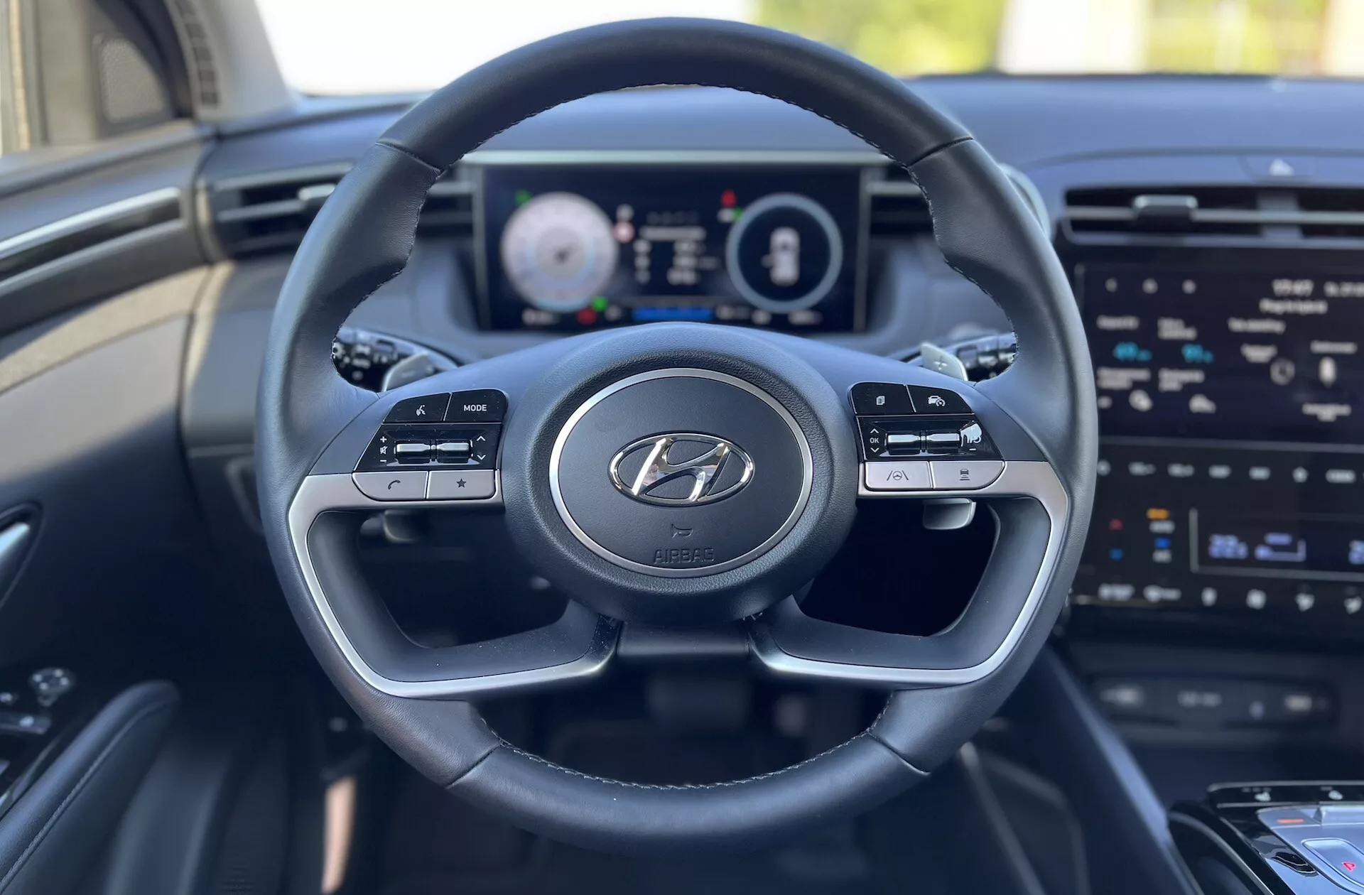 Vista interna della Hyundai Tucson 2020 dal sedile del conducente che mostra il volante con logo Hyundai, il cruscotto digitale e lo schermo dell'infotainment