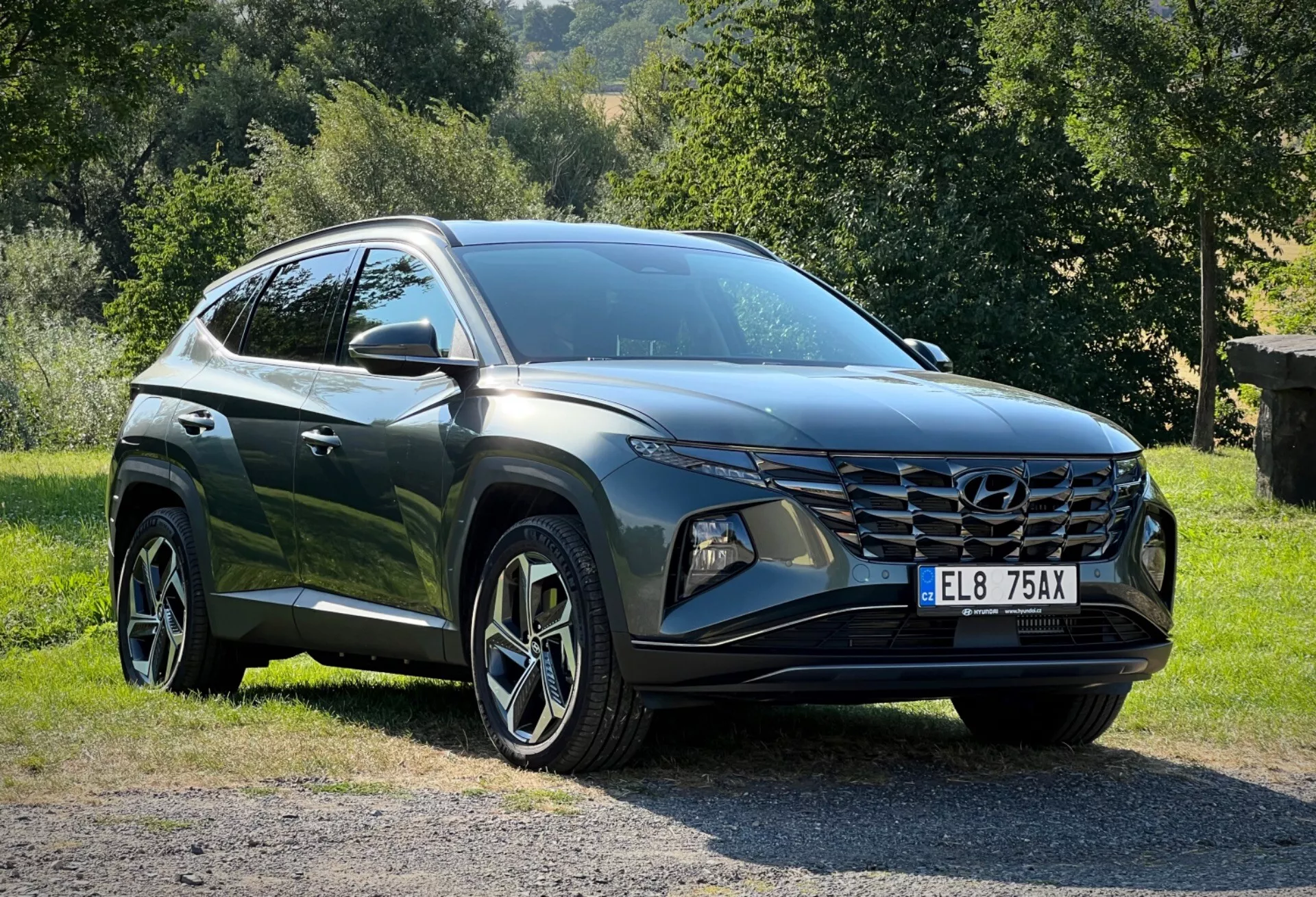Hyundai Tucson 2020 parcheggiata sull'erba con sfondo di campagna, mostrando prospettiva frontale ai tre quarti per una vista dettagliata dei suoi eleganti fari LED, griglia frontale angolare e finitura lucida di colore scuro