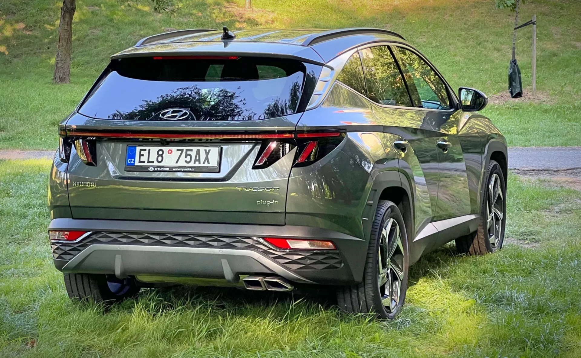 Vista posteriore tre quarti di un Hyundai Tucson 2020 che mostra le sue luci posteriori LED, design aerodinamico con spoiler sul tetto e antenna a pinna di squalo, finitura premium verde metallico scuro, e dotato di grandi ruote in lega e sensori di parcheggio, in un contesto crossover urbano