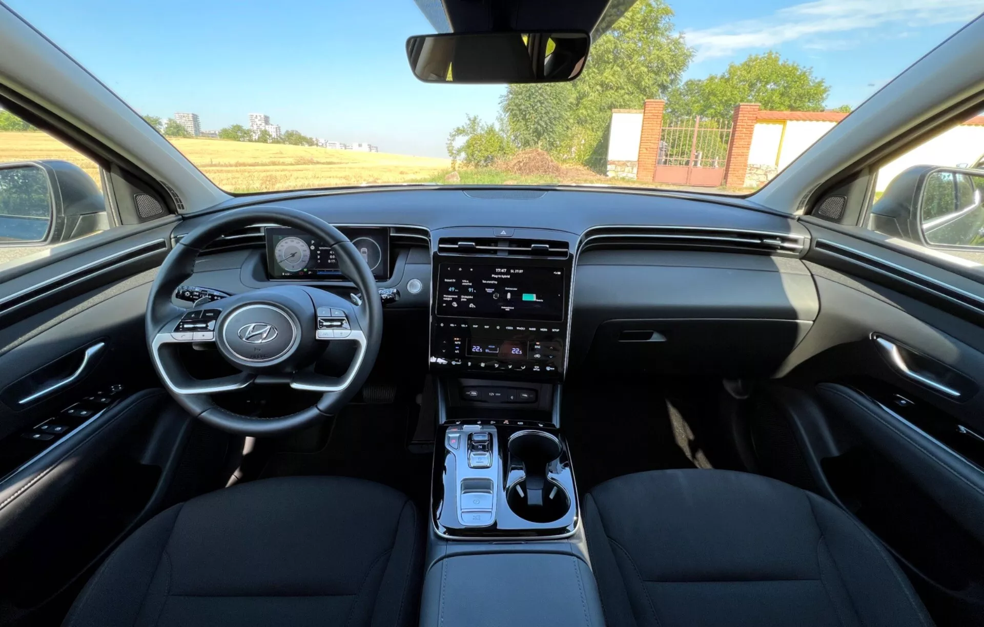Interno della Hyundai Tucson 2020 che mostra i sedili anteriori, il volante con logo del produttore e pulsanti di controllo, cluster strumenti digitale, sistema di infotainment touchscreen verticale sulla console centrale, leva del cambio automatico, e design del cruscotto bicolore da una prospettiva a livello degli occhi che ricorda quella del guidatore o del passeggero anteriore