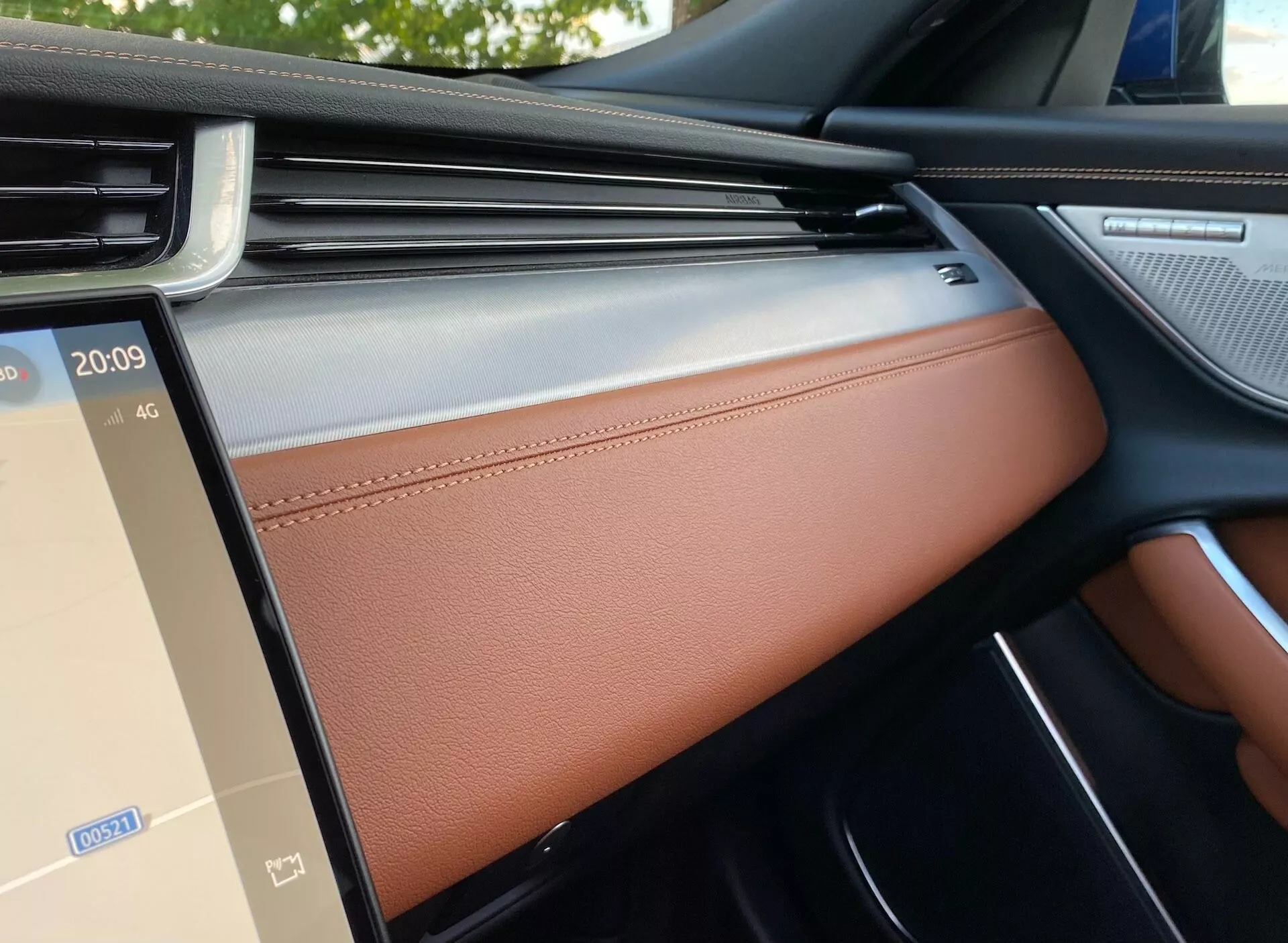 Vista interna della Jaguar XF 2021 dal sedile anteriore del passeggero, che mostra il lato destro del cruscotto, lo schermo dell'infotainment e la porta del passeggero. Le caratteristiche includono una griglia di ventilazione con finitura cromata, schermo dell'infotainment touch integrato che mostra l'ora e il segnale 4G, finiture in legno, pelle con cuciture e finiture nere lucide, riflettendo un design lussuoso e una tecnologia avanzata.