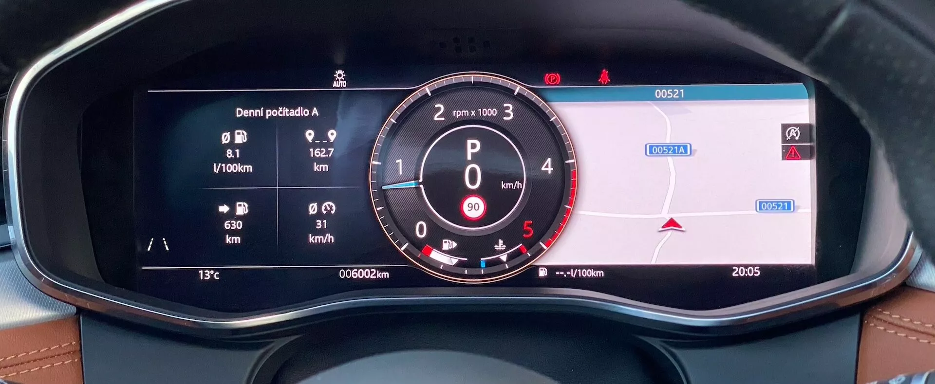 Vista ravvicinata dal sedile del conducente del quadro strumenti digitale della Jaguar XF 2021, che presenta metriche di consumo di carburante, un tachimetro analogico con RPM e tachimetro digitale, informazioni di navigazione, contachilometri, temperatura esterna e orario visualizzati. Il quadro strumenti è incorniciato da una plancia con cuciture in pelle, evidenziando gli aspetti di lusso e tecnologia degli interni del veicolo.