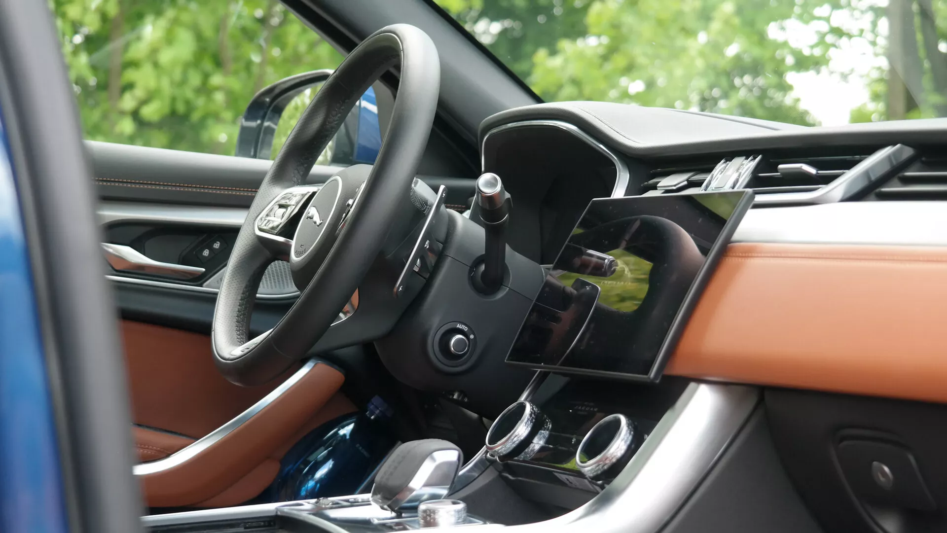 Interni lussuosi della Jaguar XF 2021 con rivestimenti in pelle beige chiaro, cruscotto decorato in legno, sistemi moderni di infotainment e controllo del clima e volante multifunzione, visto da un'angolazione laterale esterna.