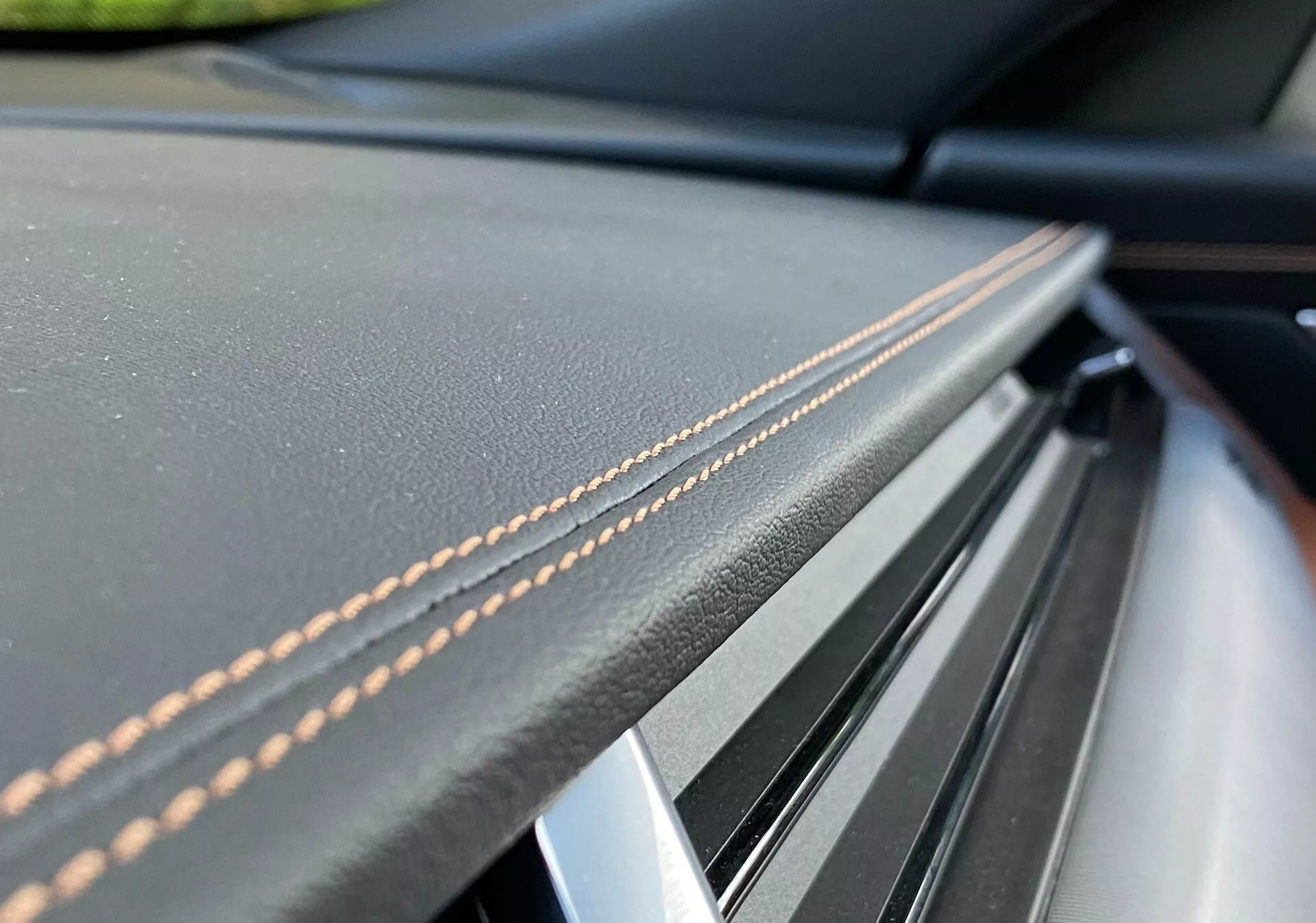 Immagine ravvicinata del dettaglio dell'interno della Jaguar XF 2021, con pelle di alta qualità cucita e un sottile pezzo trim lucido sul cruscotto o sul pannello della porta. Le cuciture meticolose e i materiali di lusso sono evidenziati dalla ridotta profondità di campo, sottolineando artigianalità ed eleganza.