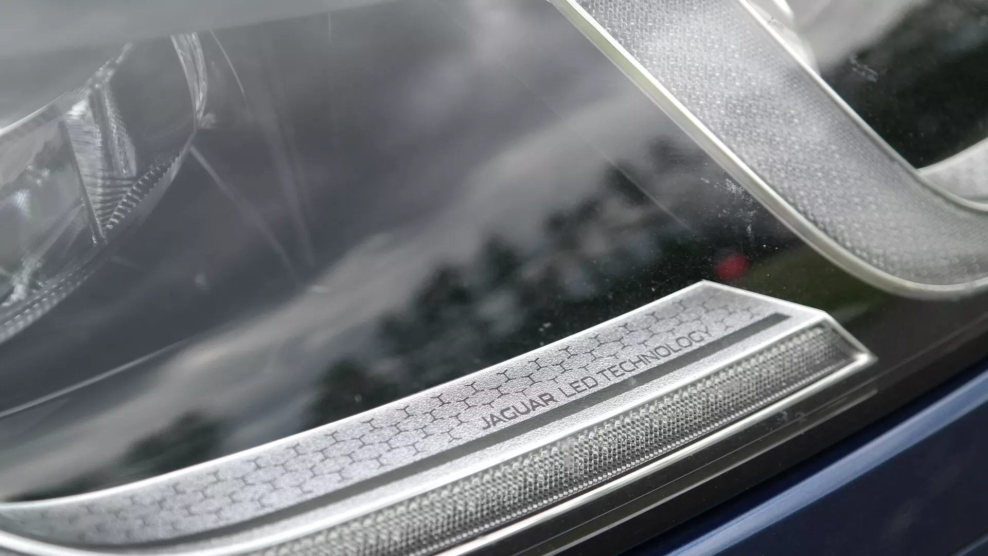 Particolare del faro della Jaguar XF 2021 con l'iscrizione 'Jaguar LED Technology', che mostra l'illuminazione LED avanzata, il design di lusso e l'artigianato dettagliato con uno sfondo sfocato che enfatizza l'array complesso del faro.