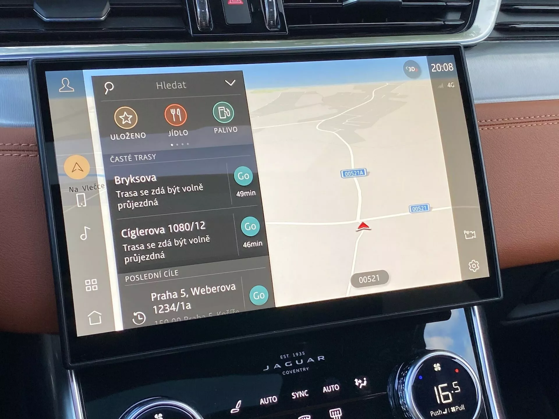 Vista interna dello schermo dell'infotainment della Jaguar XF 2021 che mostra un'interfaccia touchscreen bilingue con mappa di navigazione a destra e controlli multimediali a sinistra, circondata da pulsanti e quadranti del climatizzatore, che indica caratteristiche tecnologiche di lusso.