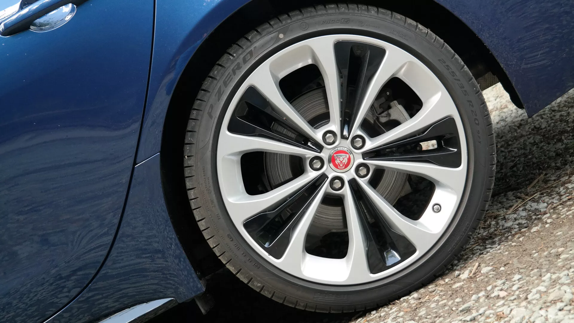 Vista ravvicinata della ruota anteriore lato guida della Jaguar XF 2021 da un'angolazione bassa che mostra un elegante design a raggi multipli in lega con finiture metalliche argentate e più scure, dettagli del battistrada del pneumatico e finitura della vernice metallica riflettente sulla parte inferiore del pannello laterale della vettura.