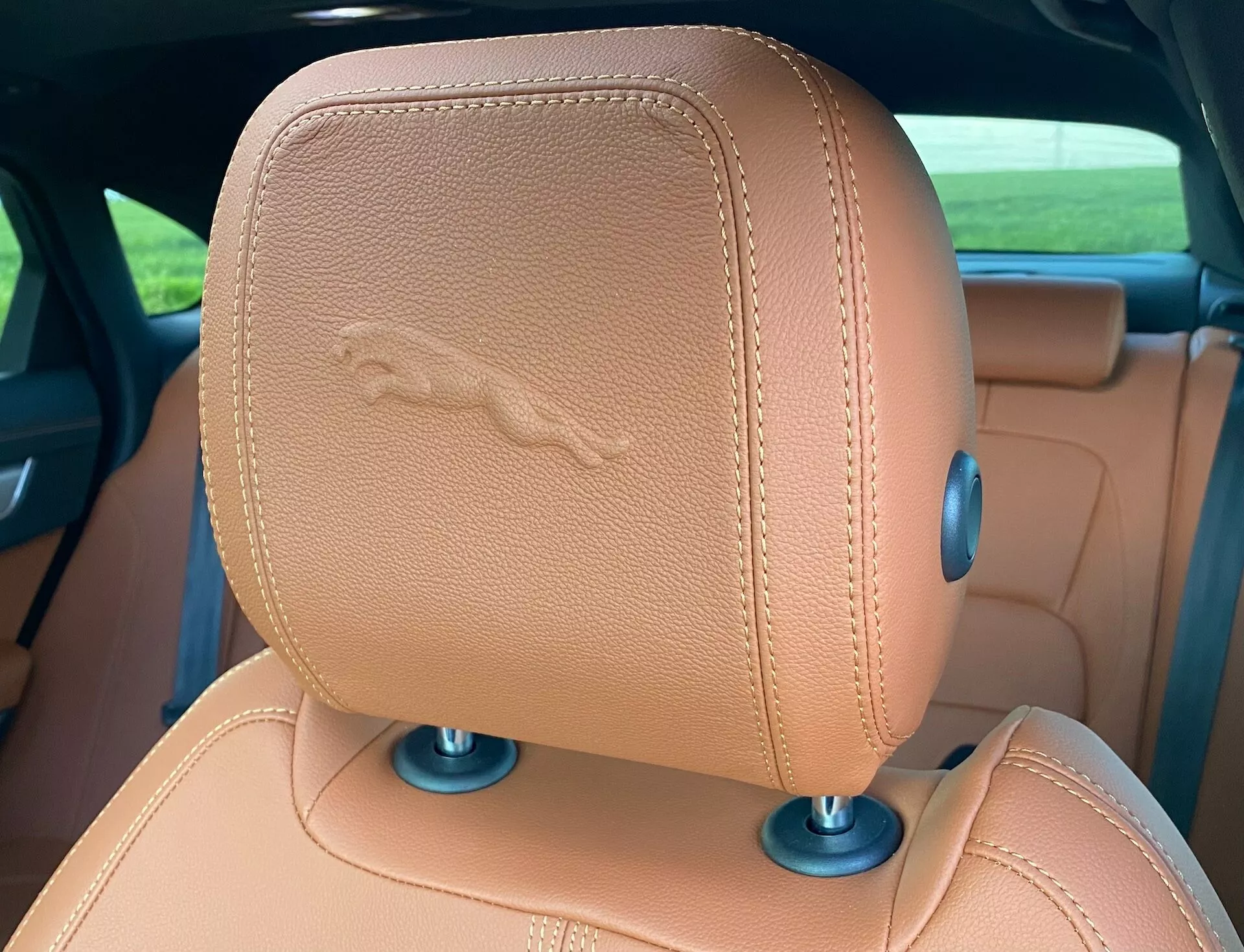 Vista ravvicinata del poggiatesta del sedile posteriore della Jaguar XF 2021, con pelle color cuoio e stemma cucito con cavallo, suggerendo caratteristiche di lusso. Gli elementi circolari blu alla base indicano possibili meccanismi regolabili.
