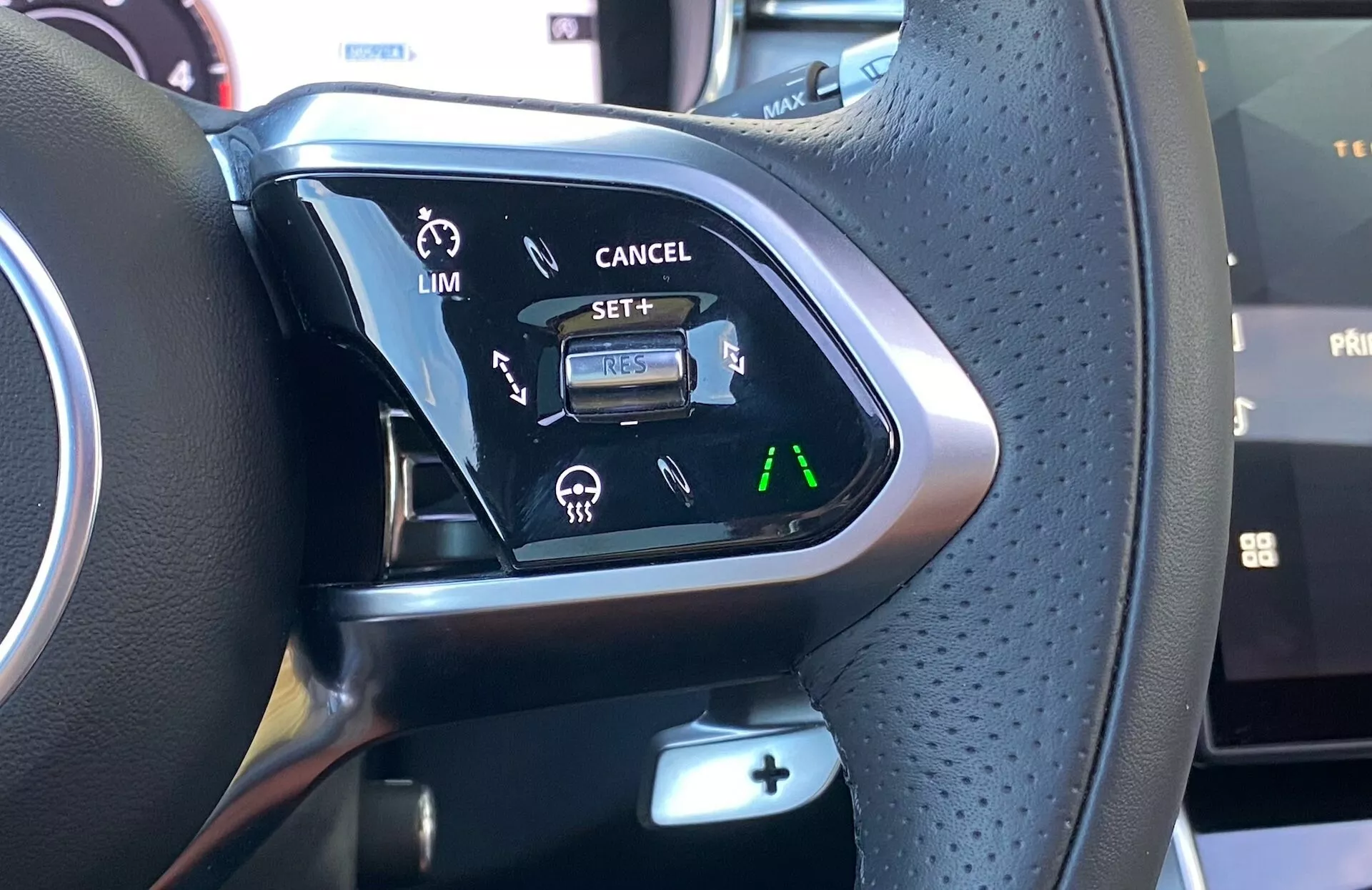 Primo piano dei comandi del volante della Jaguar XF 2021, che presenta un cambio multifunzione con pelle traforata per una migliore presa, accenti in metallo o legno e una varietà di pulsanti di controllo. Le caratteristiche visibili includono le impostazioni di assistenza alla guida per limitatore di velocità e cruise control con illuminazione per la visibilità in condizioni di scarsa illuminazione.