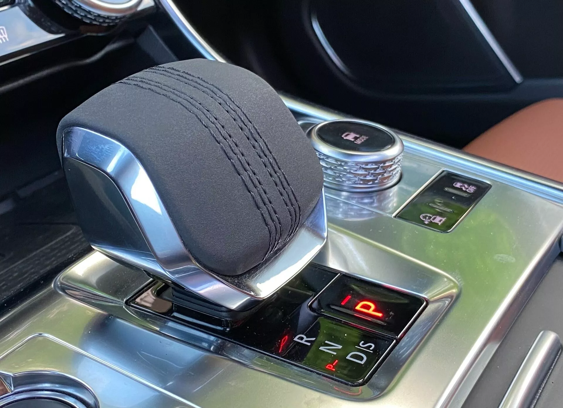 Primo piano dell'area del cambio dell'interno della Jaguar XF 2021, che mostra un elegante selettore di marcia elettronico shift-by-wire con posizioni del cambio illuminate, e una consolle centrale con finitura effetto legno lucido con funzionalità avanzate tra cui controllo di trazione, freno di stazionamento elettronico e disattivazione del sistema Auto Start/Stop.