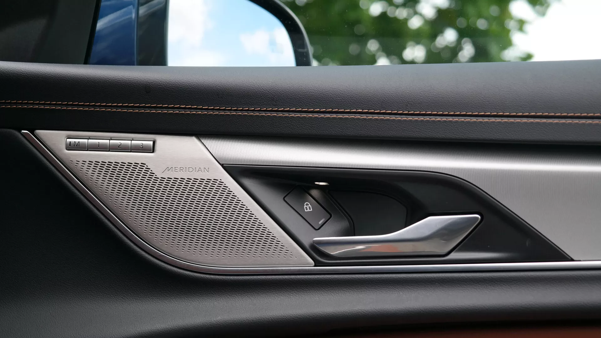 Immagine ravvicinata del pannello interno della portiera della Jaguar XF 2021 che mostra un sistema audio di alta qualità Meridian, una maniglia della portiera sofisticata, un pulsante del sistema di chiusura centralizzata e un bracciolo in pelle lussuosamente cucito, evidenziando la tecnologia avanzata e i materiali premium dell'auto.