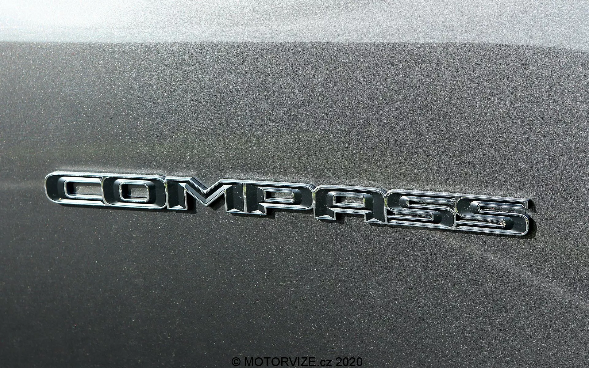 Vista ravvicinata del badge Jeep Compass 2017 con iscrizione lucida e cromata contro il pannello di carrozzeria testurizzato.
