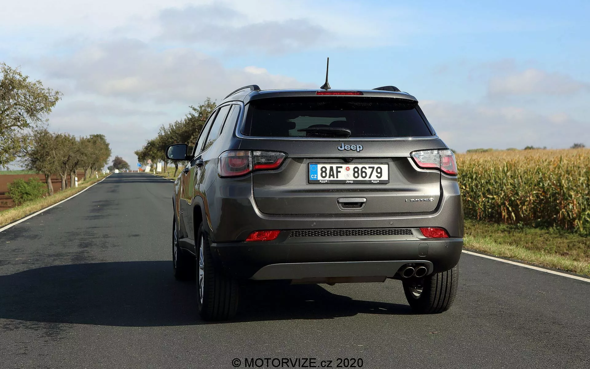 Vista posteriore a tre quarti di una Jeep Compass 2017 che mostra elementi di design distintivi tra cui fanali posteriori, paraurti posteriore, sistema di scarico doppio, marchi sulla parte posteriore del cofano, tergicristallo posteriore, striscia riflettente, cerchi in lega a cinque razze, antenna montata sul tetto e riflettori sul bordo inferiore. L'immagine fornisce una prospettiva chiara da dietro e leggermente dal lato del conducente con ampio spazio tra l'auto e la fotocamera.
