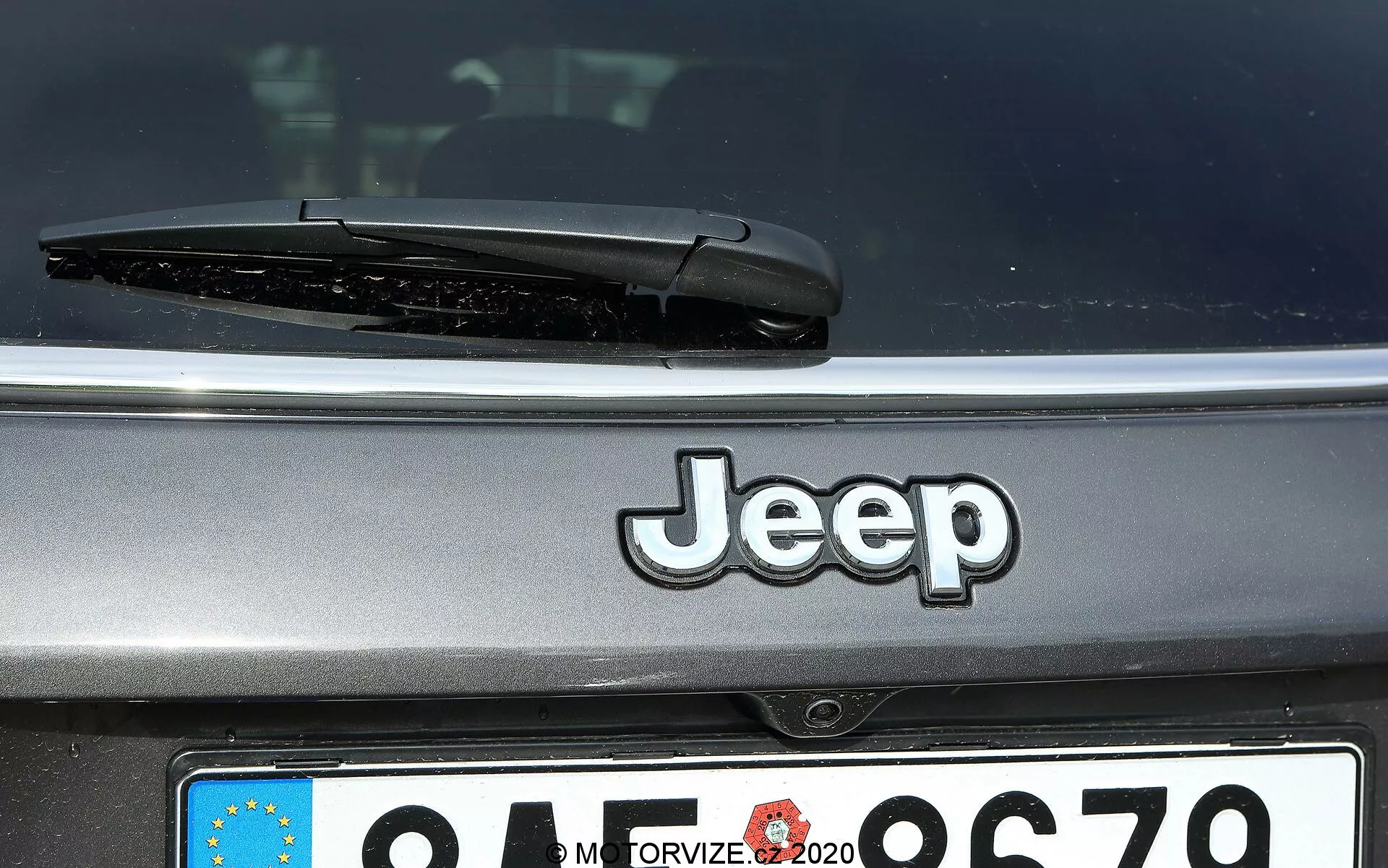 Vista ravvicinata della parte posteriore di una Jeep Compass 2017 che mostra il logo Jeep centrato, il tergicristallo posteriore e una targa in stile europeo parzialmente visibile con l'identificatore del paese sfocato
