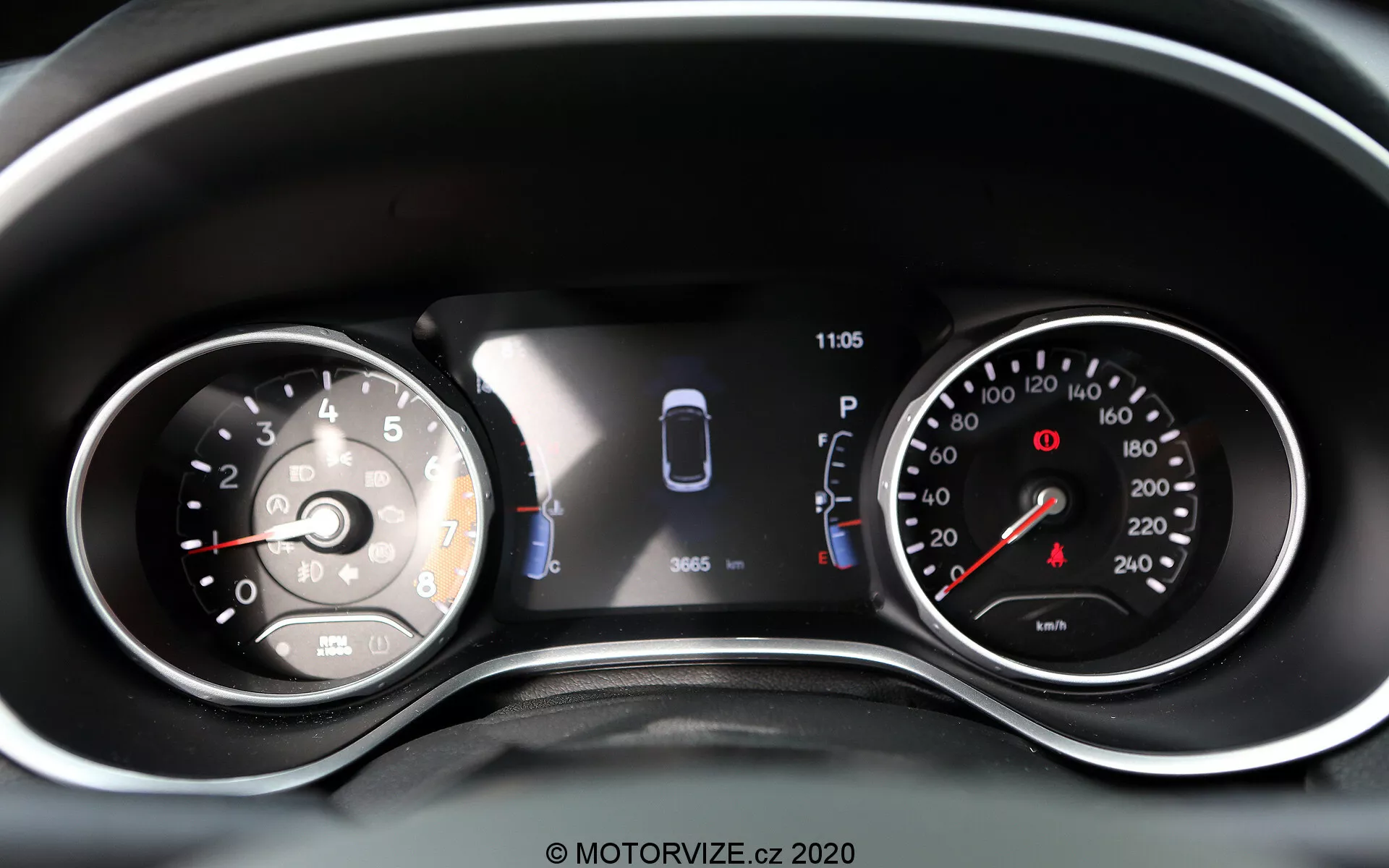 Vista ravvicinata del quadro strumenti della Jeep Compass 2017 con una combinazione di quadranti analogici e display digitale. A sinistra c'è un tachimetro analogico segnato fino a 260 con l'ago che punta appena sopra lo 0. Il display digitale centrale include un grafico dell'auto con sensori e due porte aperte, indicando l'assistenza al parcheggio e lo stato del veicolo. Un orologio mostra le 11:05. A destra c'è un contagiri analogico con zona rossa che inizia prima di 7, segnato fino a 8 (incrementi di 1.000 giri/min). Sono visibili ulteriori spie di avvertimento e icone, facendo di questo una rappresentazione ben illuminata e chiara delle letture moderne e tradizionali del veicolo e delle tecnologie di assistenza alla guida.
