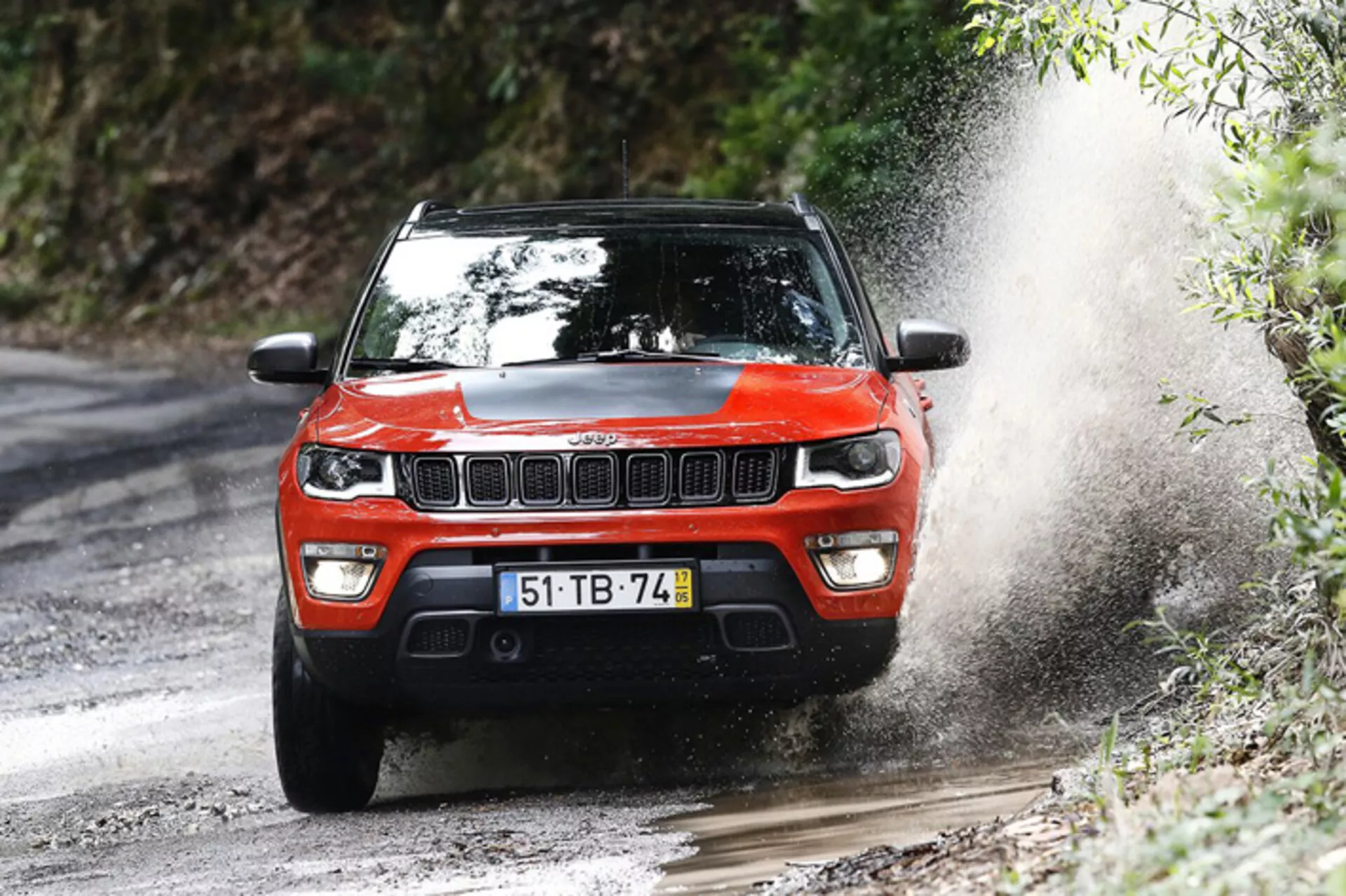 SUV Jeep Compass 2017 in azione dinamica fuoristrada, mostrato da un angolo anteriore di tre quarti che enfatizza il suo design robusto e le capacità di prestazione su un sentiero forestale fangoso.