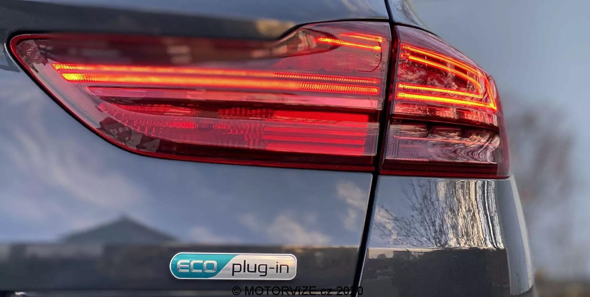 Vista ravvicinata del lato posteriore sinistro di una Kia Ceed 2018, con particolare attenzione al gruppo di luci posteriori illuminate con un design multistrato. Il badge 'ECO plug-in' indica che si tratta di un veicolo ibrido plug-in. La finitura lucida e il coperchio del bagagliaio leggermente visibile aggiungono dettagli al design complessivo dell'auto.