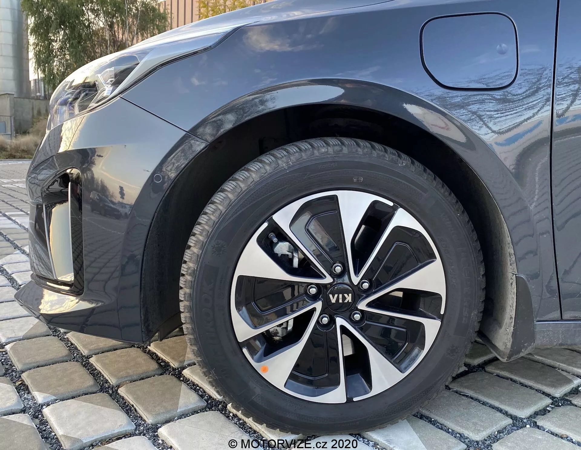 Primo piano con inquadratura a bassa angolazione della ruota anteriore destra di una KIA Ceed 2018, con un design in lega multirazza in nero e argento, con visibili motivi del battistrada, che mostra parzialmente il parafango anteriore, il paraurti e parte del cofano in un colore metallico scuro.
