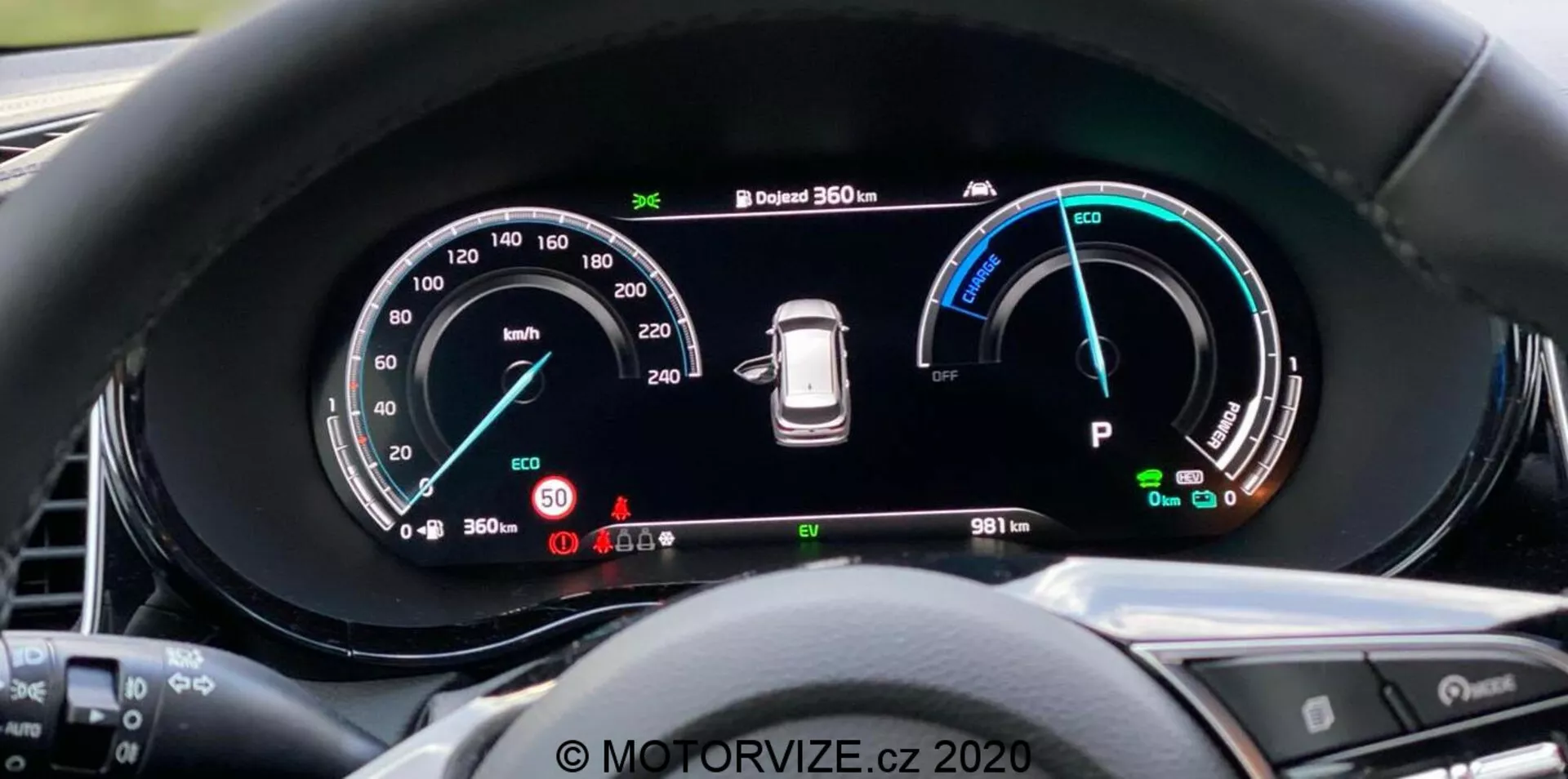 Vista ravvicinata del quadro strumenti digitale della Kia Ceed 2018 dalla prospettiva del conducente, con un ampio display panoramico e strumentazione dettagliata che include un tachimetro fino a 260 km/h, un indicatore di potenza con modalità Eco, Comfort e Power, un'avviso di pressione dei pneumatici e un'indicatore della modalità 'Park'. Il quadro strumenti mostra anche un sistema di telecamere a 360 gradi e un odometro con lettura di 9811 km. Il bordo circostante riduce l'abbagliamento e i pulsanti del volante sono parzialmente visibili. Marchio a filigrana 'MOTORVIZE.cz 2020'.
