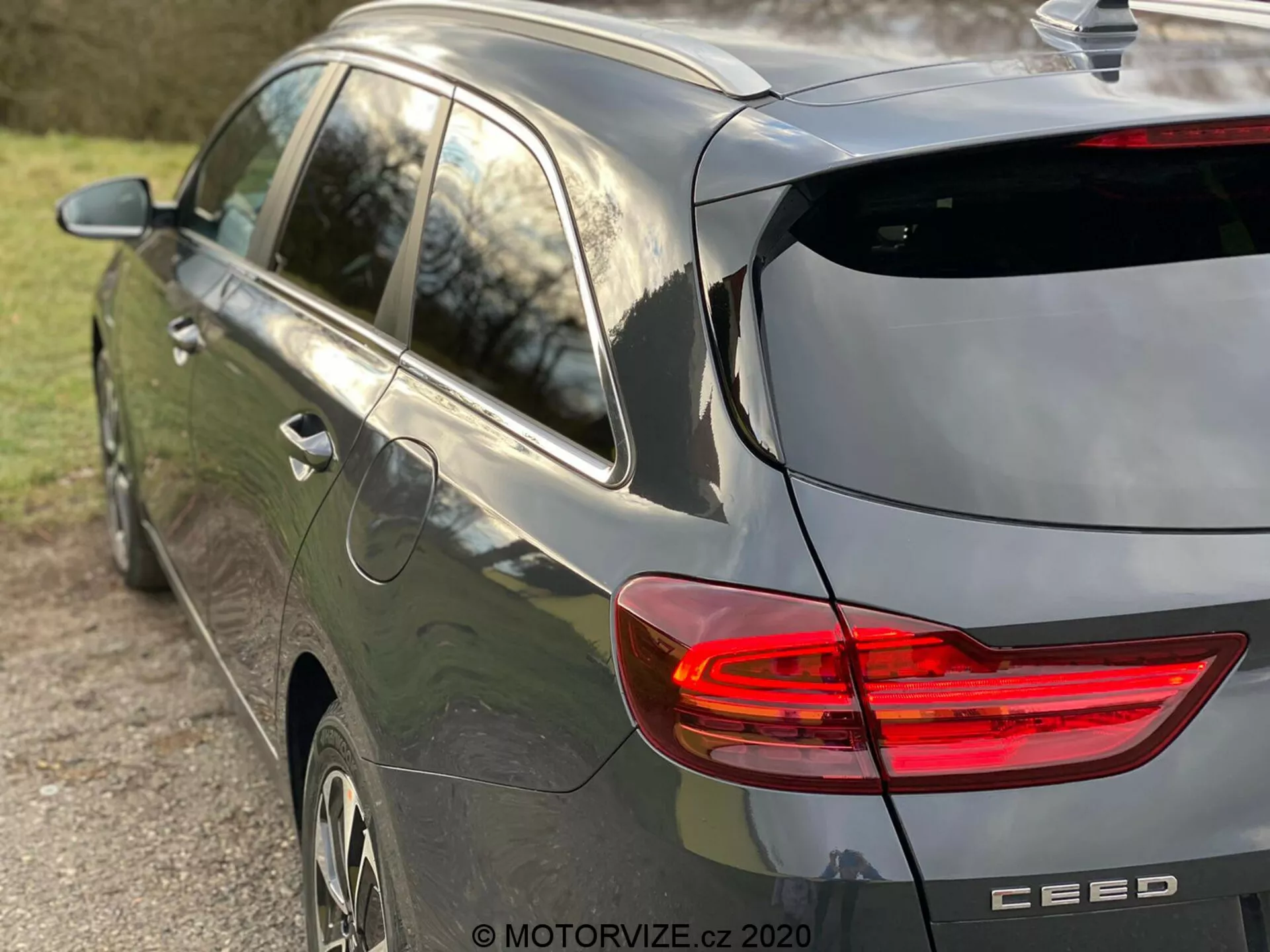 Vista parziale laterale e posteriore di una moderna hatchback grigia Kia Ceed 2018 con enfasi sulla luce posteriore a LED a forma di C illuminata, design hatchback con tergicristallo posteriore e discreto spoiler sul tetto, antenna a pinna di squalo, cerchi in lega e badge del marchio con il nome del modello 'CEED', catturata con luce naturale del tardo pomeriggio e bassa profondità di campo concentrandosi sul veicolo.