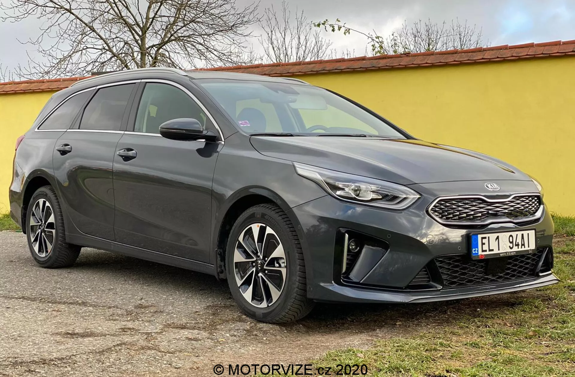 L'immagine mostra la Kia Ceed 2018, una moderna station wagon catturata da un angolo anteriore a tre quarti che mette in risalto la fascia anteriore, inclusa una griglia strutturata con un distinto emblema del marchio, fari stretti che si estendono all'indietro con luci diurne a LED e un paraurti anteriore con alloggiamenti per fendinebbia e sensori di parcheggio. Le eleganti linee di contorno del cofano conducono a un parabrezza inclinato, accentuando il profilo aerodinamico dell'auto. Sono visibili i cerchi in lega multi razze e gli specchietti laterali con indicatori di direzione integrati, insieme a una linea del tetto che digrada verso il posteriore e le barre portatutto, sottolineando sia lo stile che l'utilità. I vetri oscurati e le linee della carrozzeria lungo il lato aggiungono un aspetto scolpito. L'auto è ferma su una superficie piana all'aperto.