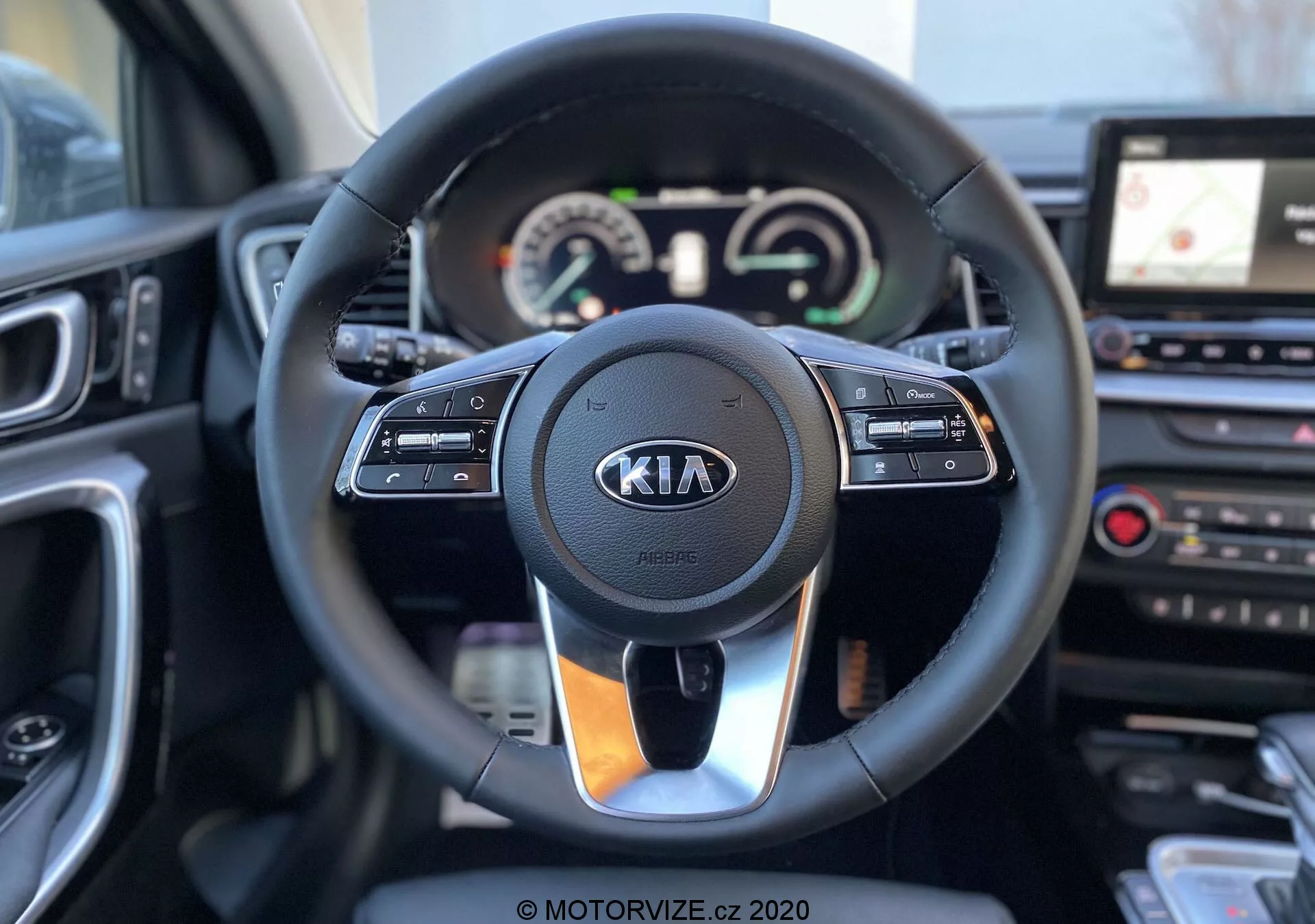 Interno di una Kia Ceed 2018 con messa a fuoco sul volante e sul cruscotto, visto dalla prospettiva del guidatore. Il moderno volante è dotato di comandi per il controllo della velocità, l'interazione multimediale e la comunicazione a mani libere, con il logo Kia ben visibile. Dietro al volante, il quadro strumenti combina quadranti analogici e un display digitale che mostra tachimetro e contagiri, insieme a un display multifunzionale. Sulla destra del volante, è visibile parte della console centrale dotata di sistema di infotainment touchscreen con navigazione GPS e comandi di climatizzazione. L'immagine è nitida, con una profondità di campo ridotta che mette in risalto il volante e i suoi dintorni immediati.