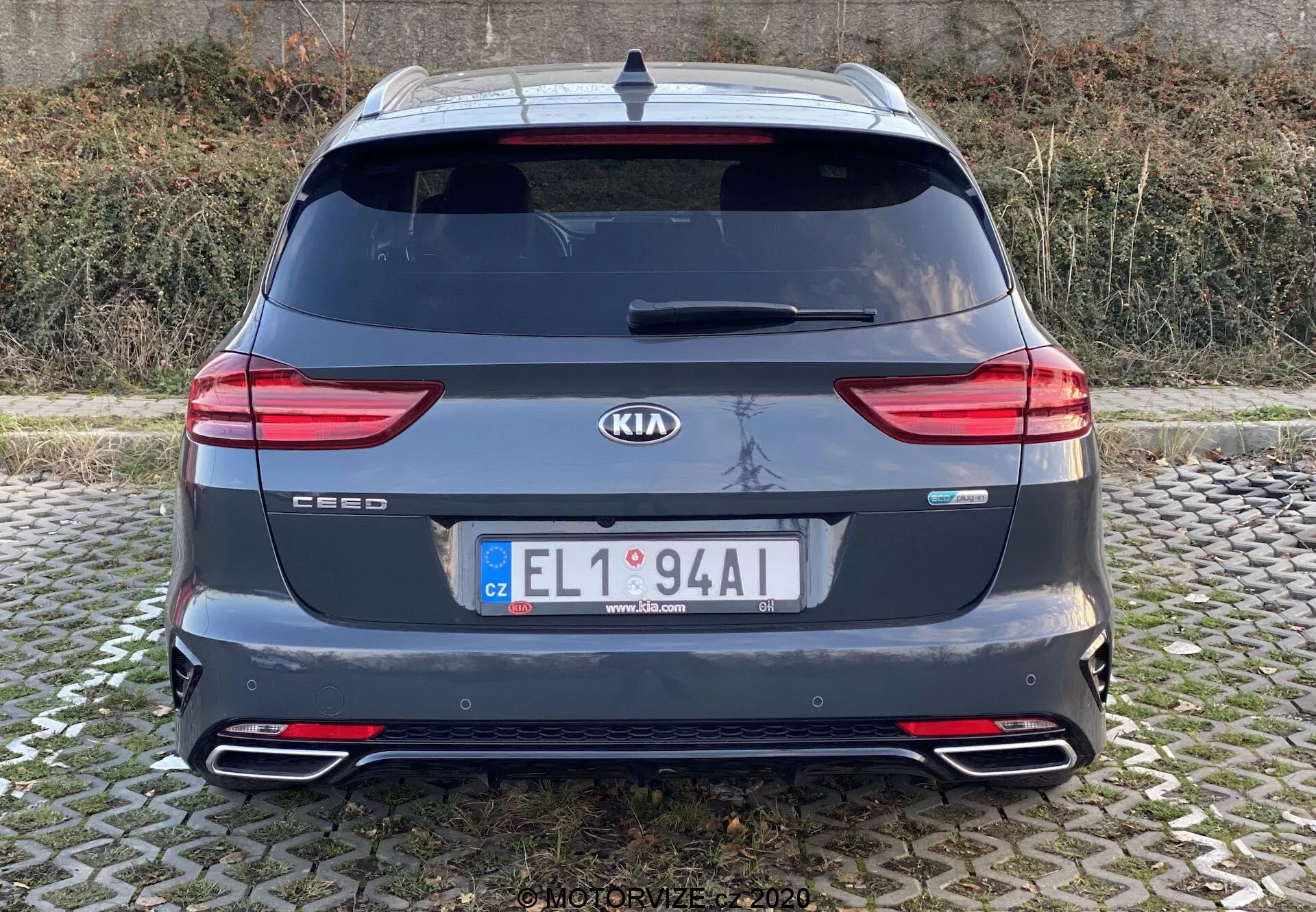 Vista posteriore di una Kia Ceed 2018 che mostra l'intera sezione posteriore con badge di marca e modello, fanali posteriori LED moderni, lunotto posteriore, doppi terminali di scarico, paraurti posteriore con riflettori, spoiler sul tetto, antenna e sensori di parcheggio posteriori. L'immagine è chiara, scattata a livello degli occhi con luce naturale in condizioni di cielo coperto.